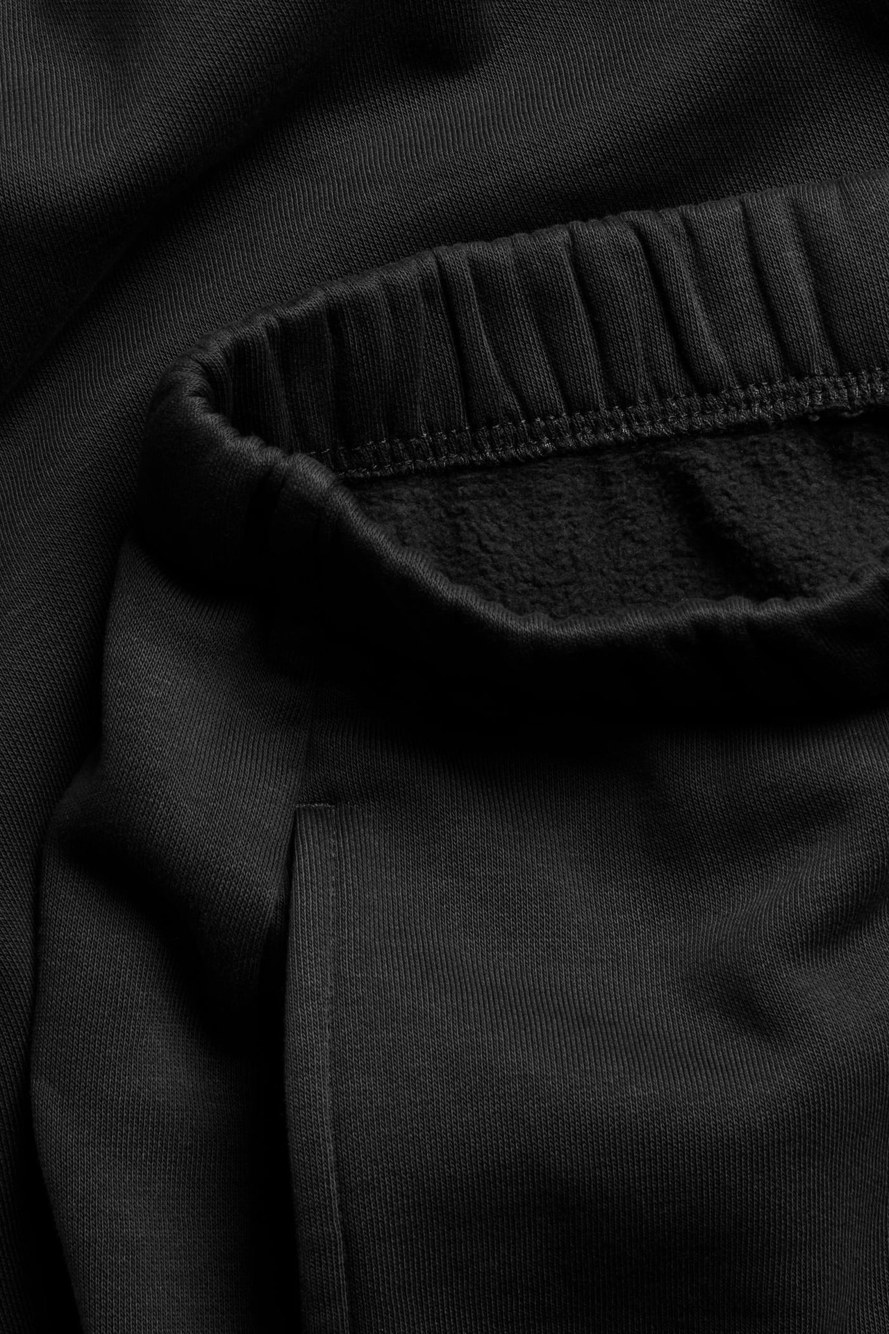 Lähikuva mustista loungewear-collegehousuista, joissa joustovyötärö ja näkyvä sivutasku.