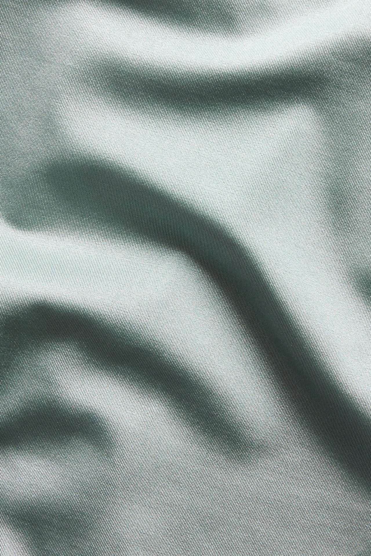 Närbild av ljusgrönt, enfärgat bikinitrosatyget med diskret textur och mjuka veck.