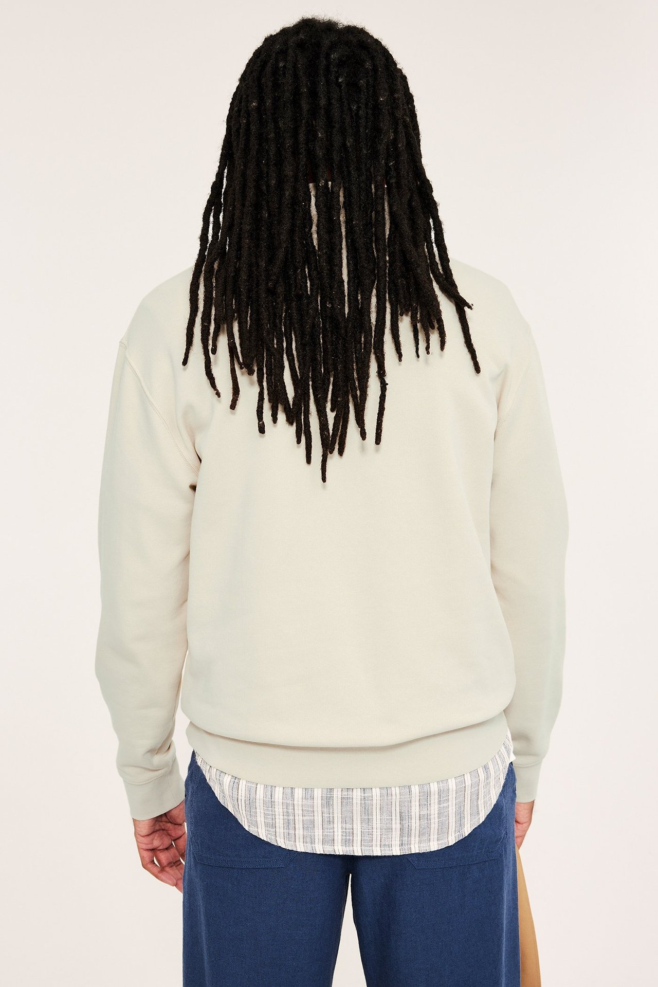 Widok z tyłu mężczyzny w jasnobeżowej bawełnianej bluzie, pod spodem pasiasta koszula i ciemnoniebieskie spodnie.