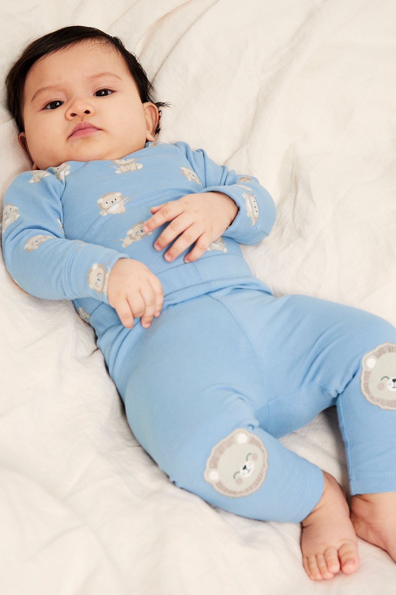 Front view: Baby i ljusblå bomullsleggings med lejonapplikationer på knäna och matchande topp med lejontryck.