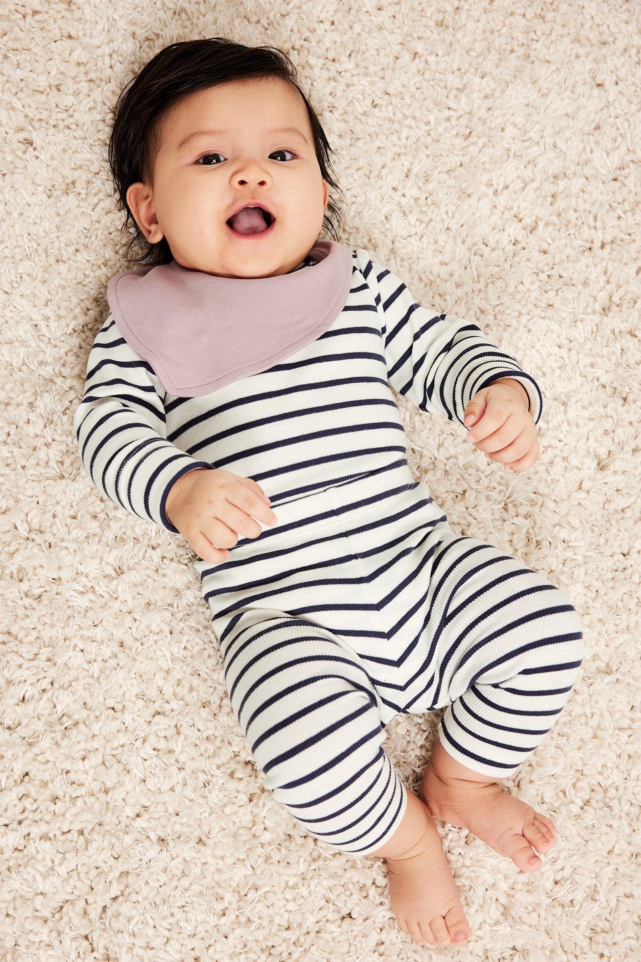 Ovenfra på baby i hvit- og marineblåstripete ribbede leggings og matchende topp, med lys lilla smekke.