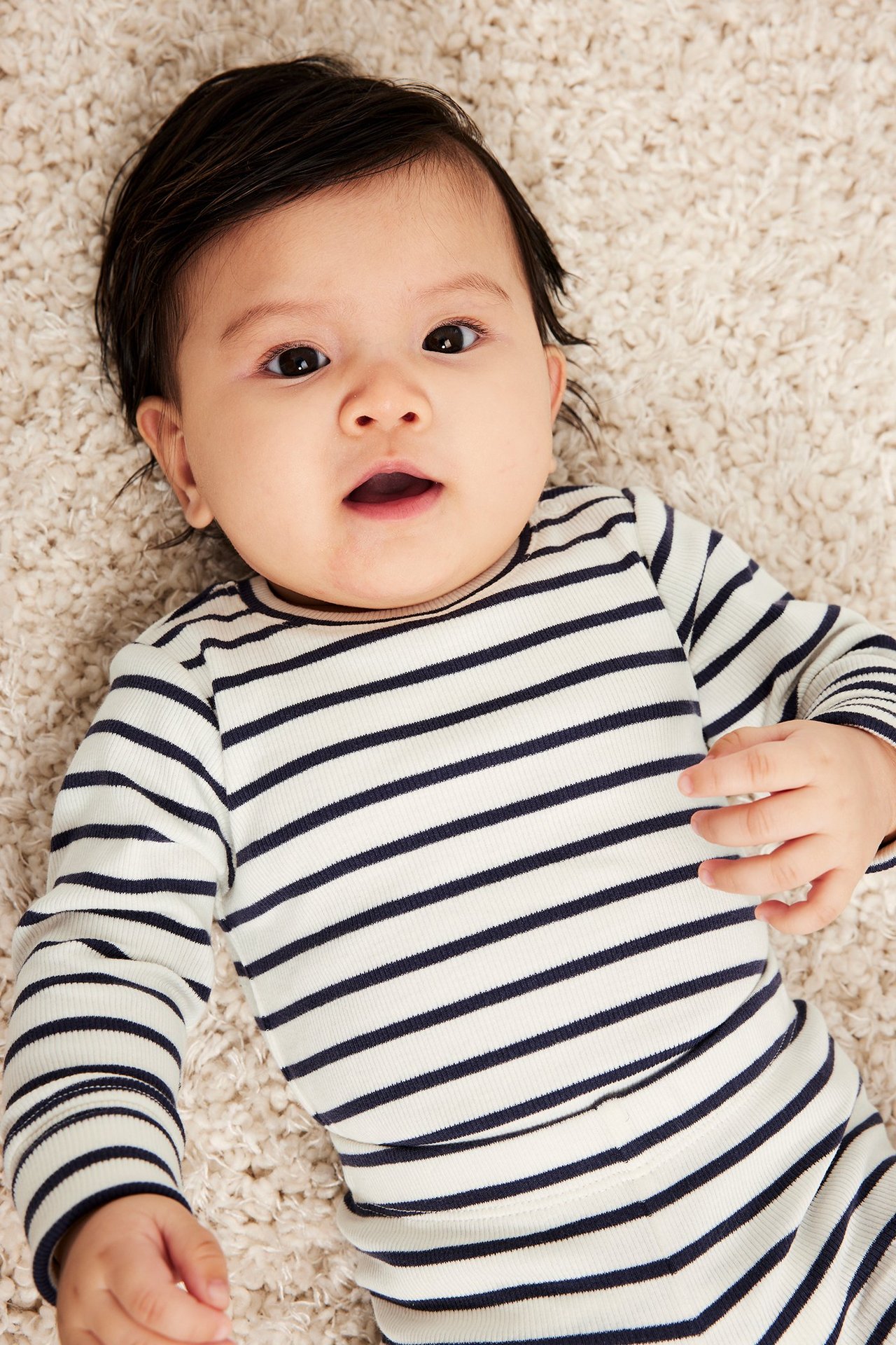 Framifrån en baby i ribbad, långärmad, benvit body med marinblå ränder.