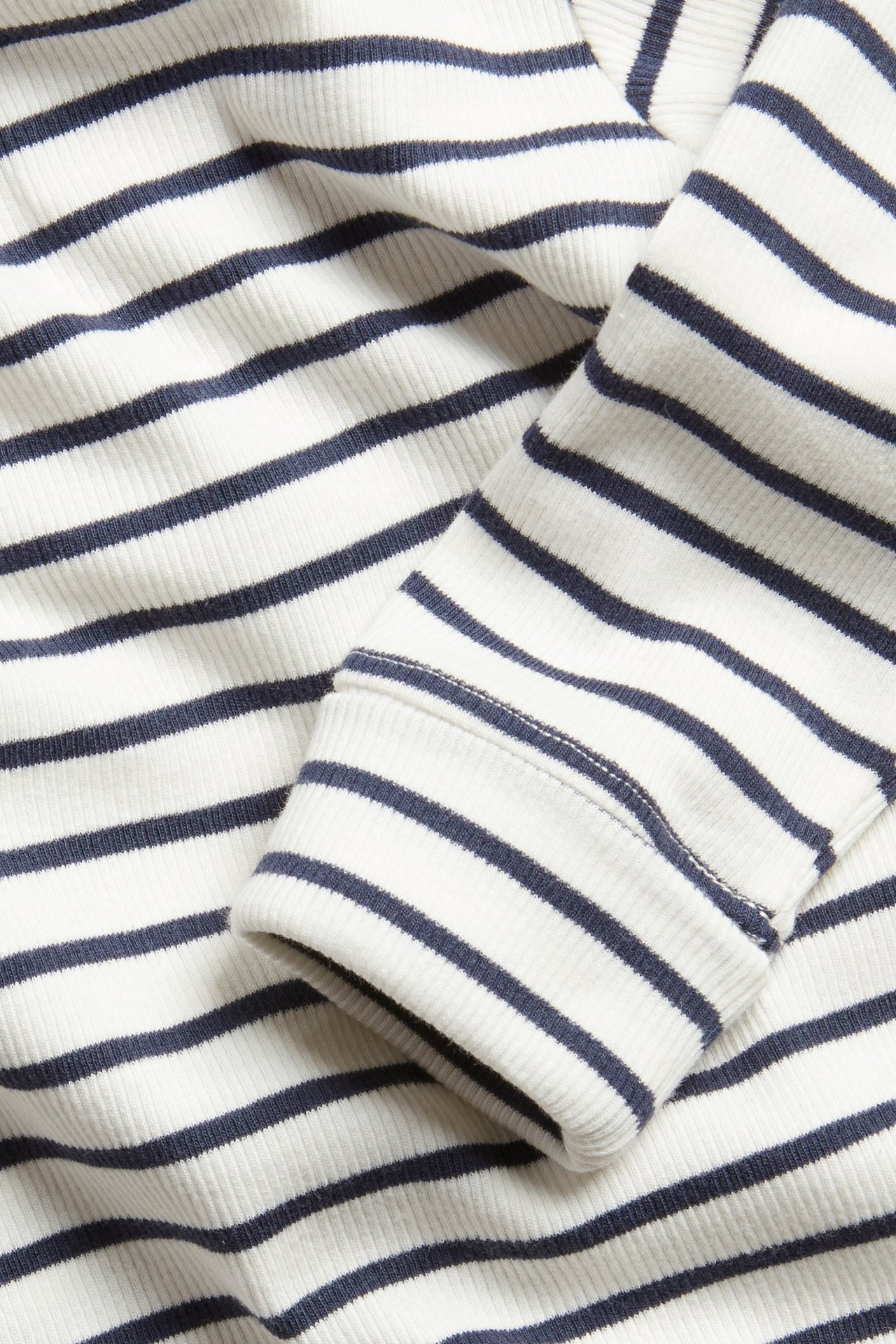 Närbild av en babys vit- och blårandiga långärmade ribbade body med mudd.