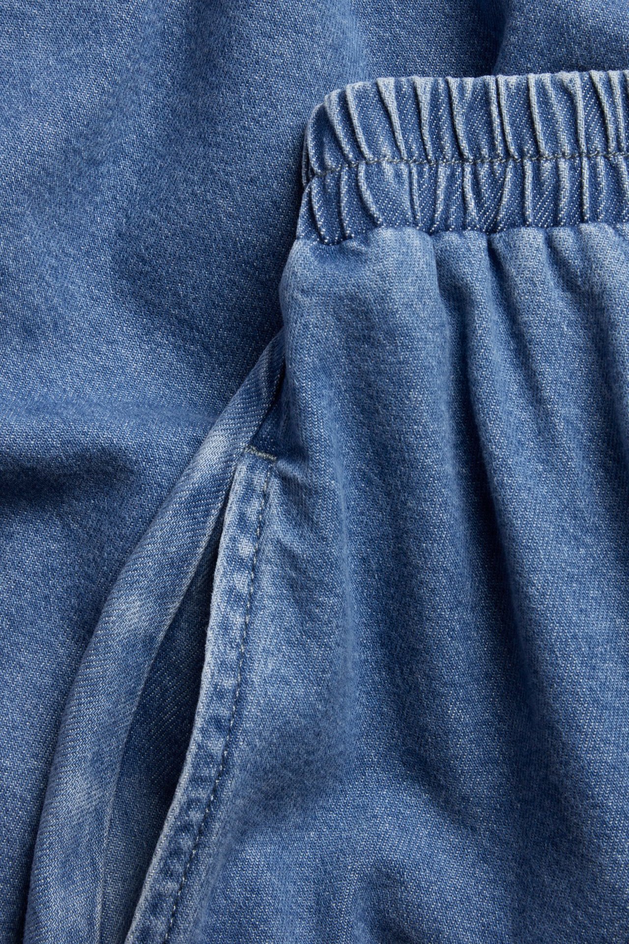 Zbliżenie niebieskiej spódnicy jeansowej z elastyczną talią i boczną kieszenią.