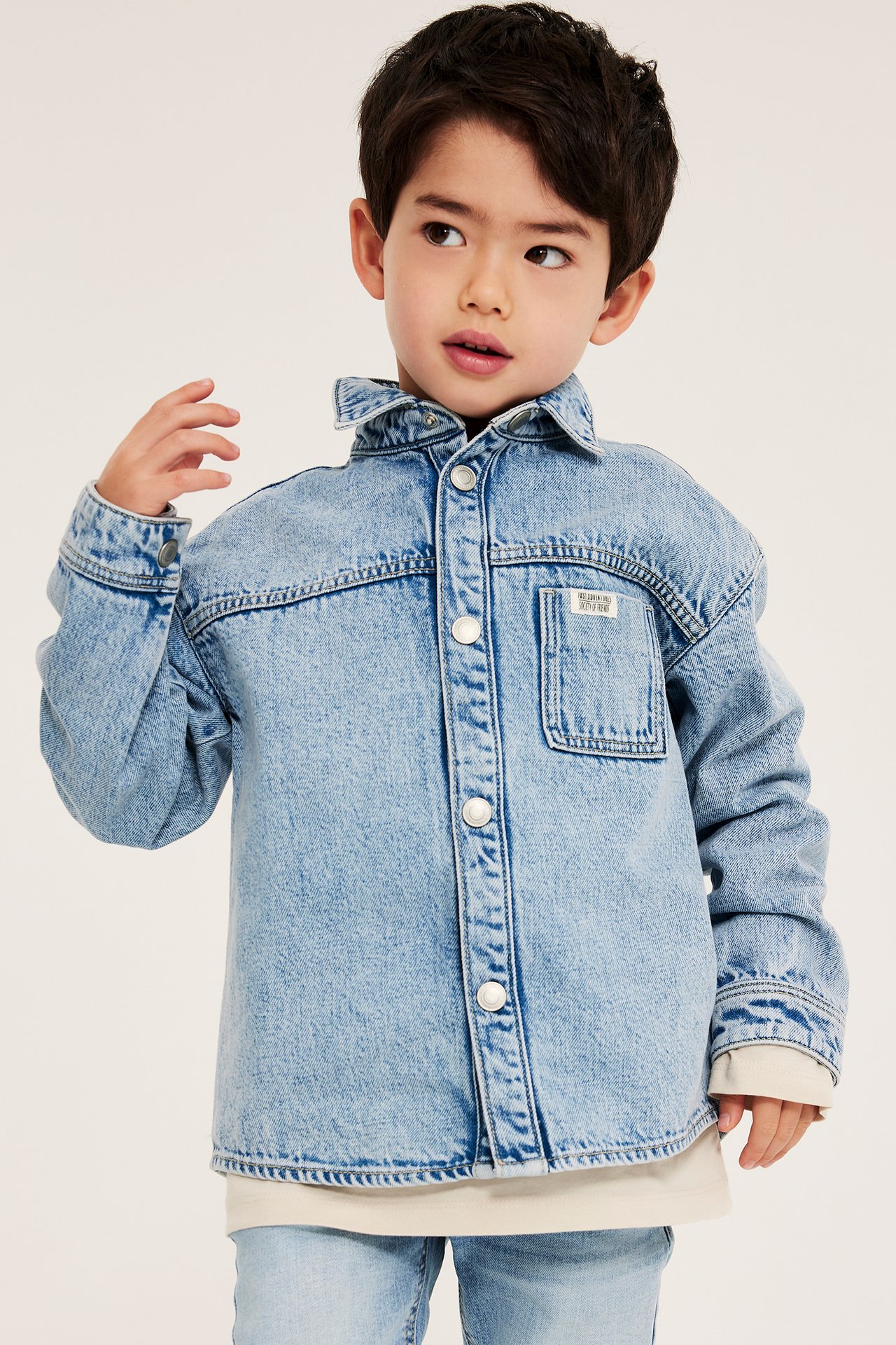 Frontbilde: Et barn i lys denim overskjorte med trykknapper, over en t-skjorte og jeans.