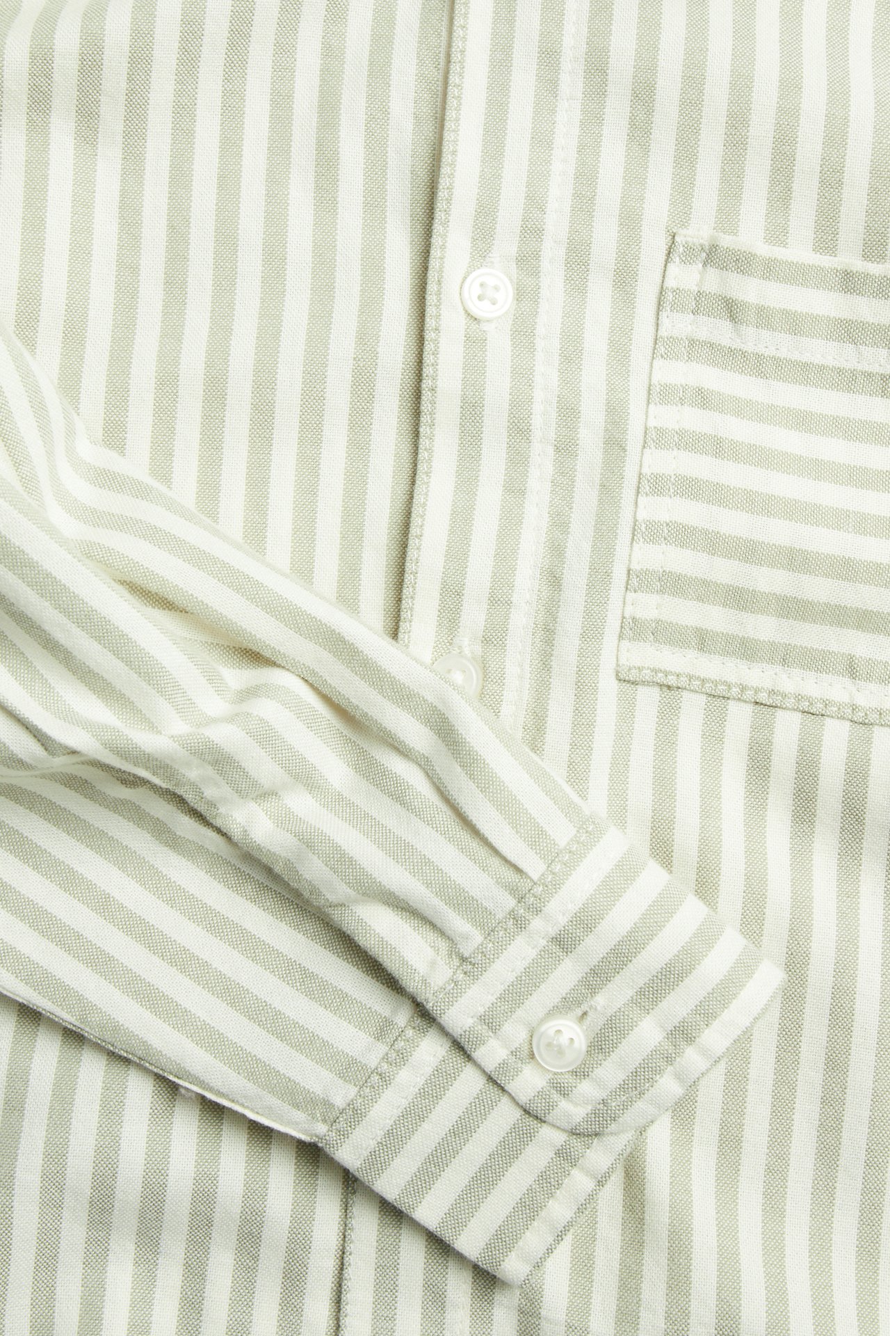 Zbliżenie dziecięcej bawełnianej koszuli w jasnozielone/białe paski z guzikami, kieszonką i mankietami.