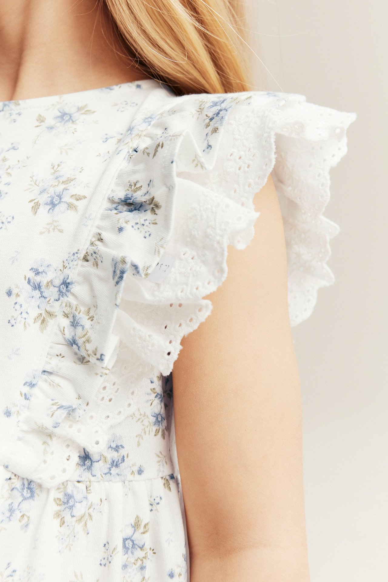 Nærbilde av barn i offwhite blomstret jerseykjole med rysjer og blondedetaljer.