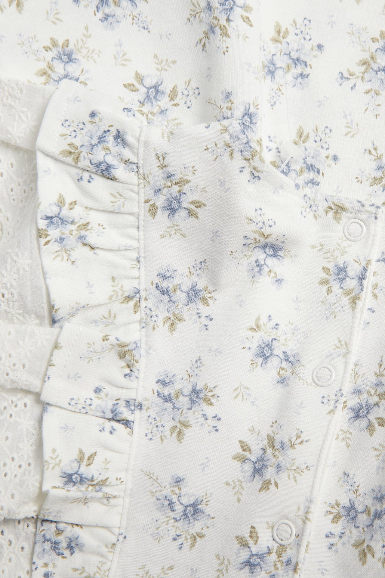 Zbliżenie: kremowobiała sukienka niemowlęca w niebieskie kwiaty, dżersej, falbanki, biała koronka, zatrzaski.