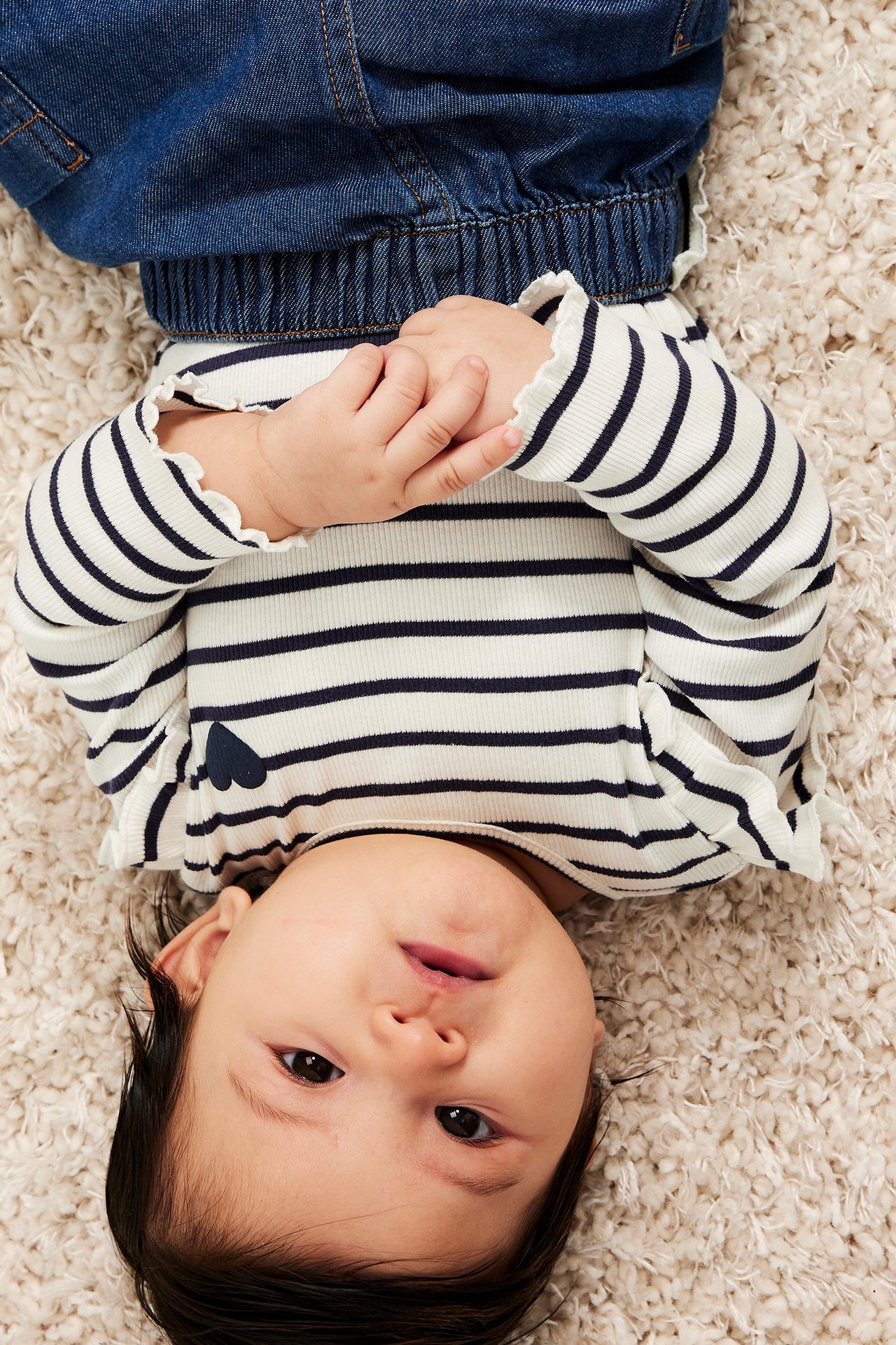 Oversikt: baby i en kremfarget, mørkeblå stripete ribbestrikket langermet topp med hjerte og blå jeans.
