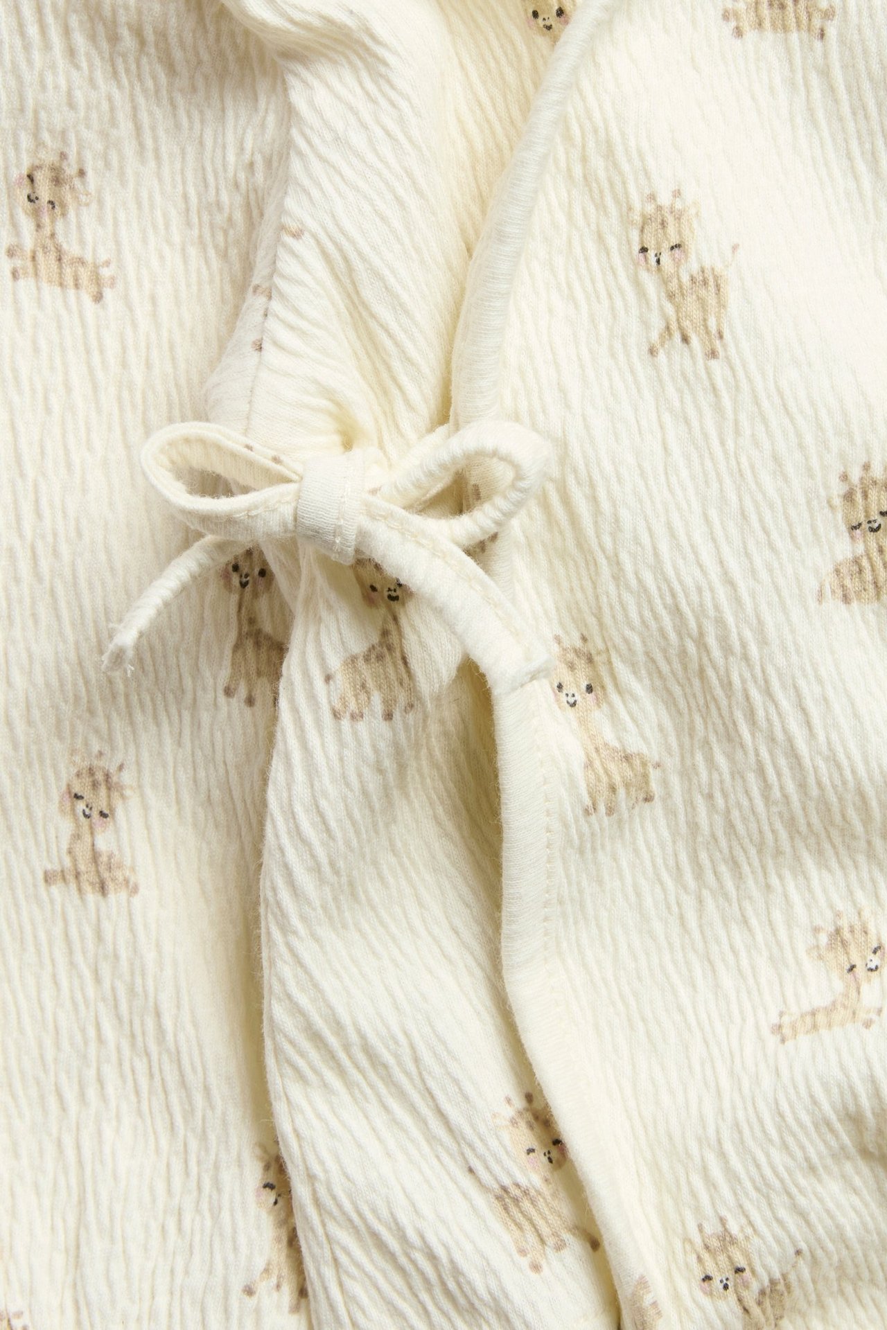 Lähikuva luonnonvalkoisesta kuvioidusta vauvan kietaisubodysta, kirahvikuviolla ja etusolmulla.