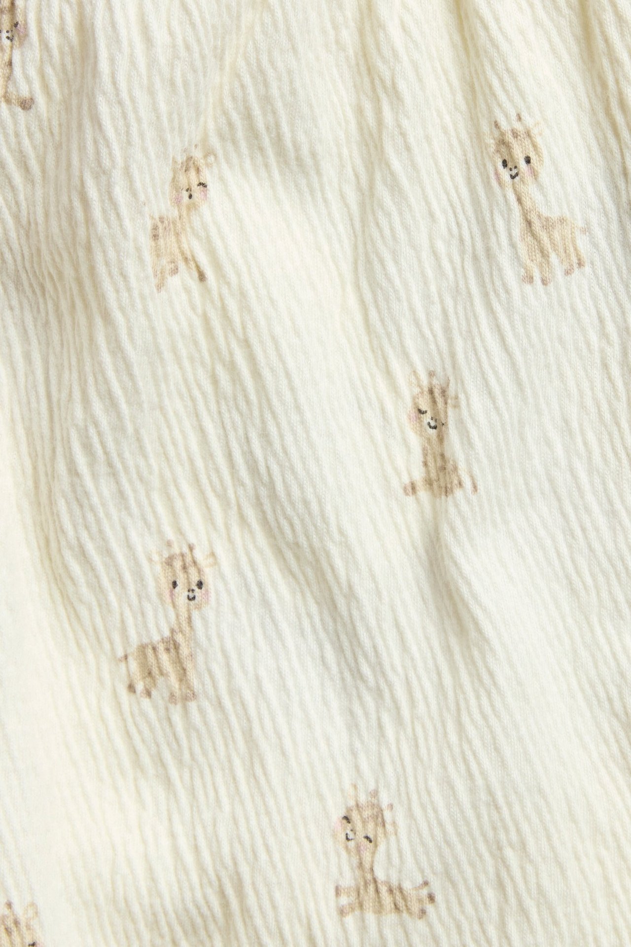 Lähikuva luonnonvalkoisesta strukturoidusta jerseykankaasta, jossa ruskea kirahvikuvio.