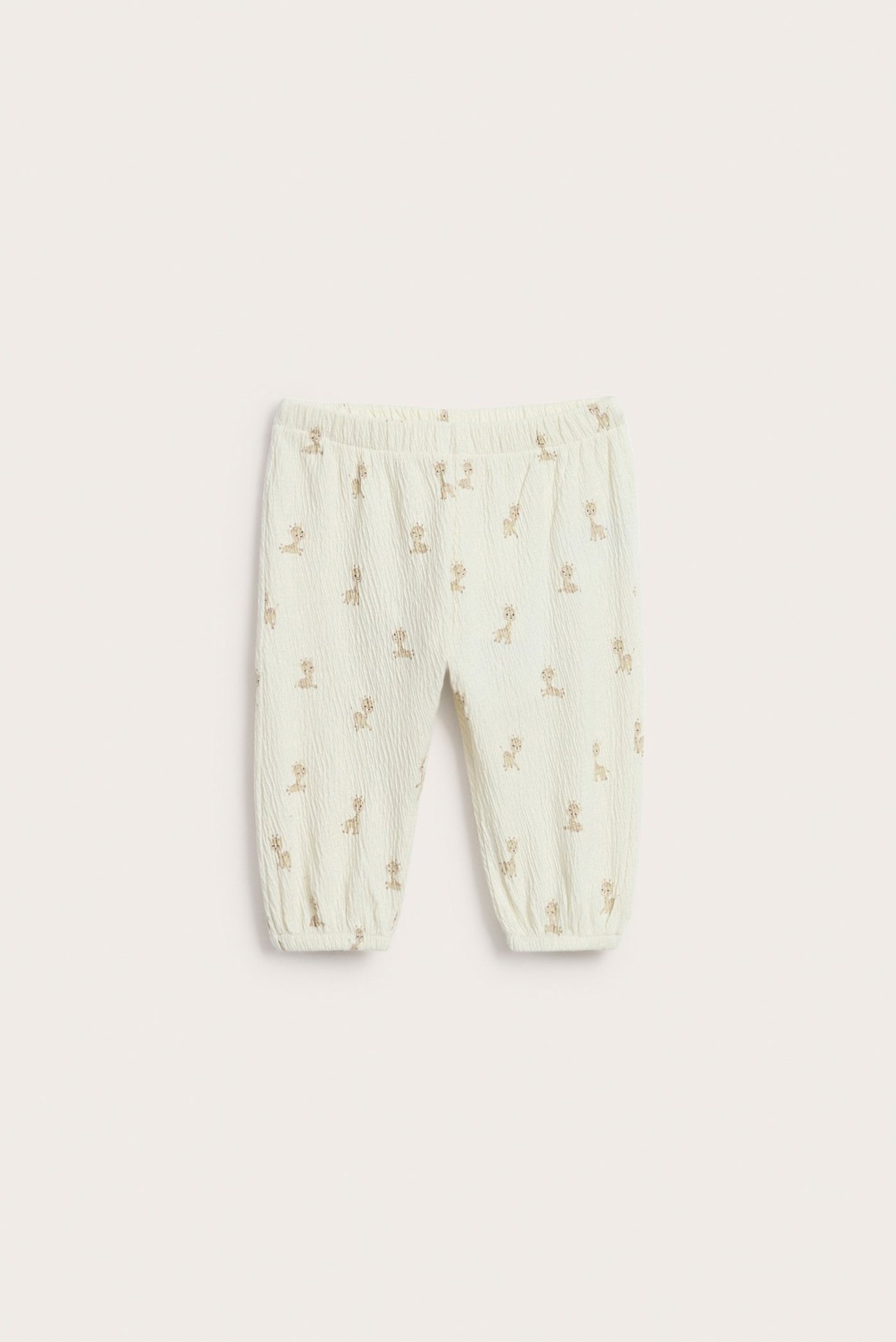 Widok z przodu: ecru spodnie niemowlęce z dżerseju, ze wzorem żyraf i elastycznymi mankietami.