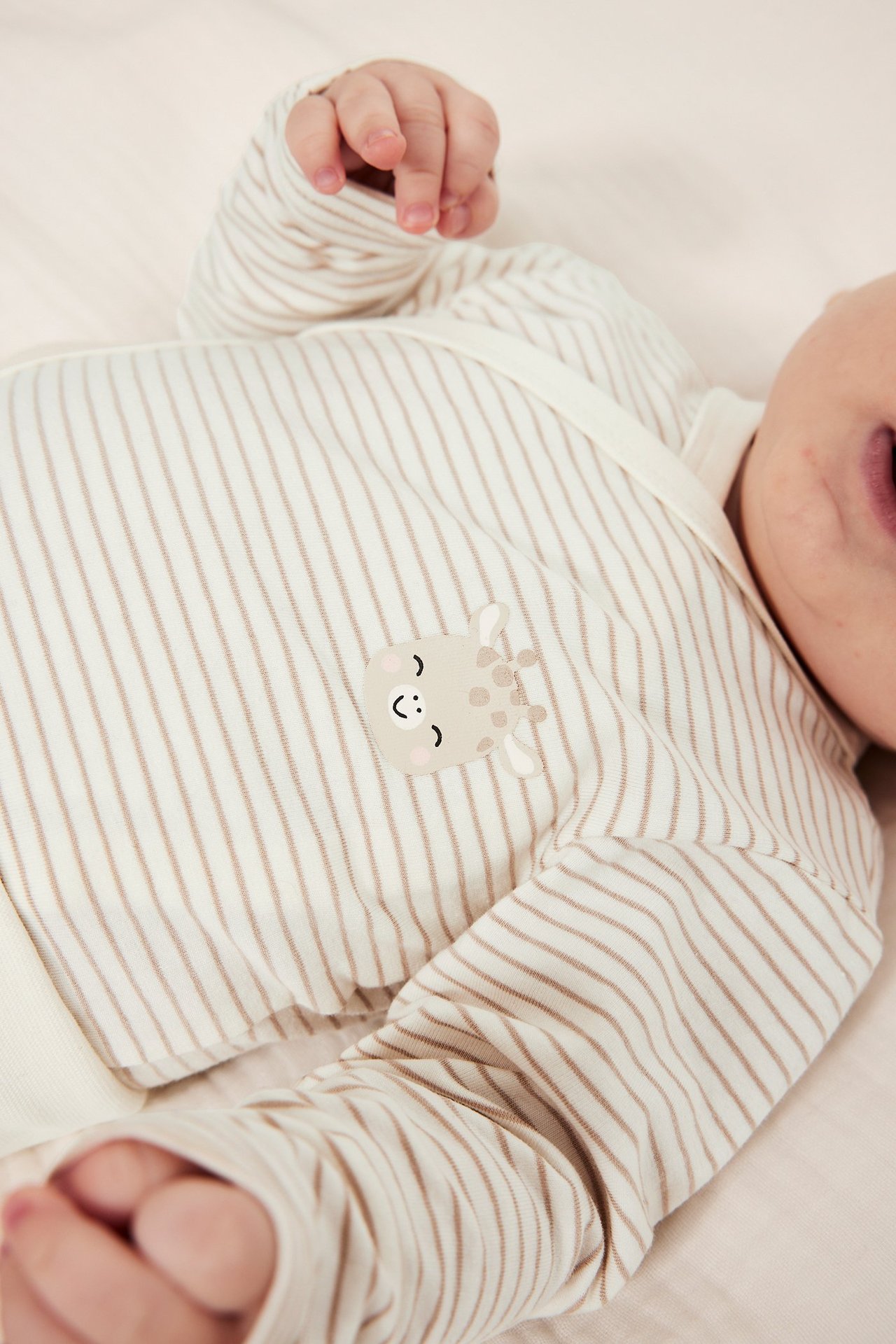 Närbild på en baby i en beige randig bomullsbody med omlottknäppning och giraffapplikation.