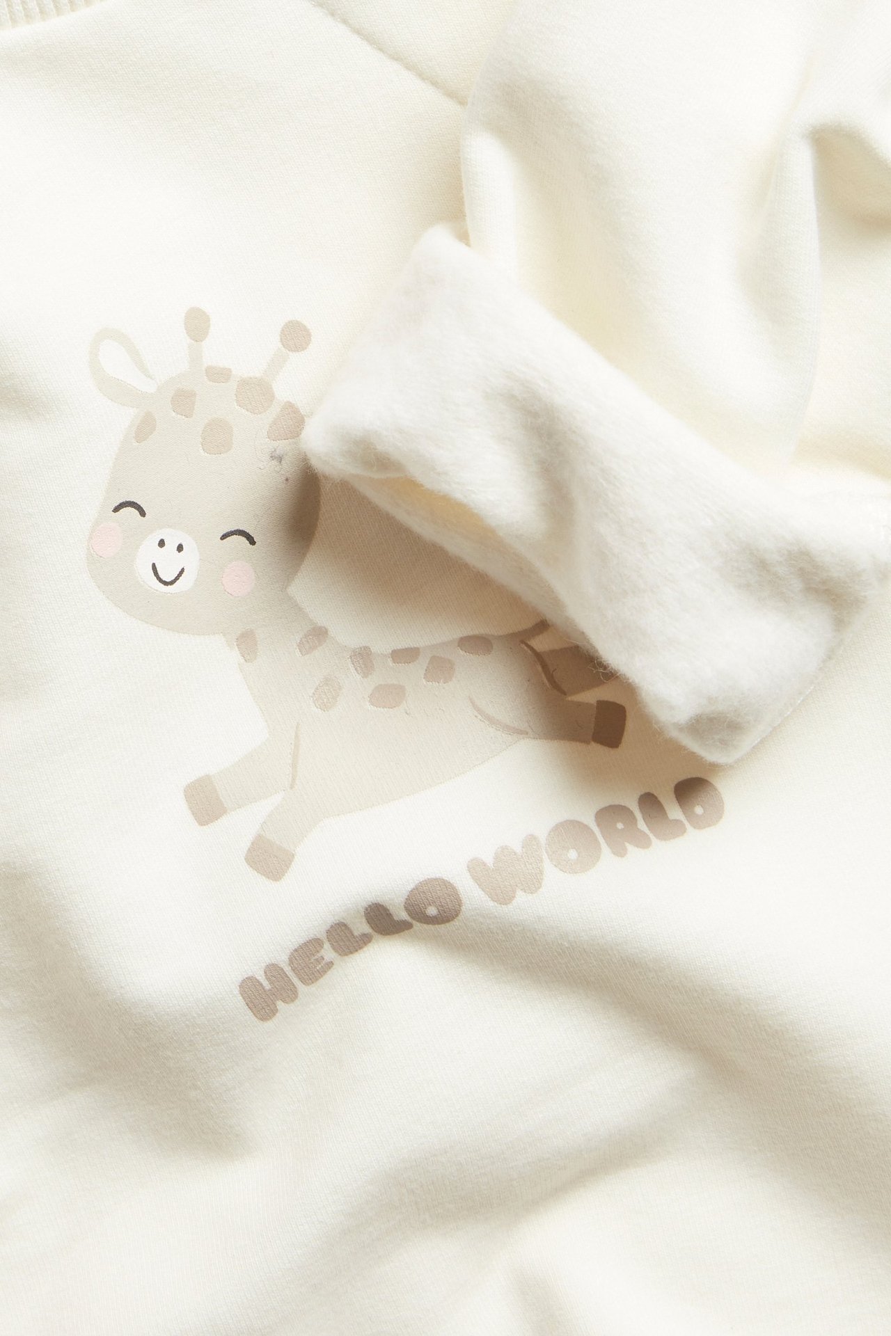 Nærbilde av en offwhite langermet babygenser med søtt sjirafftrykk og skjulte trykknapper.