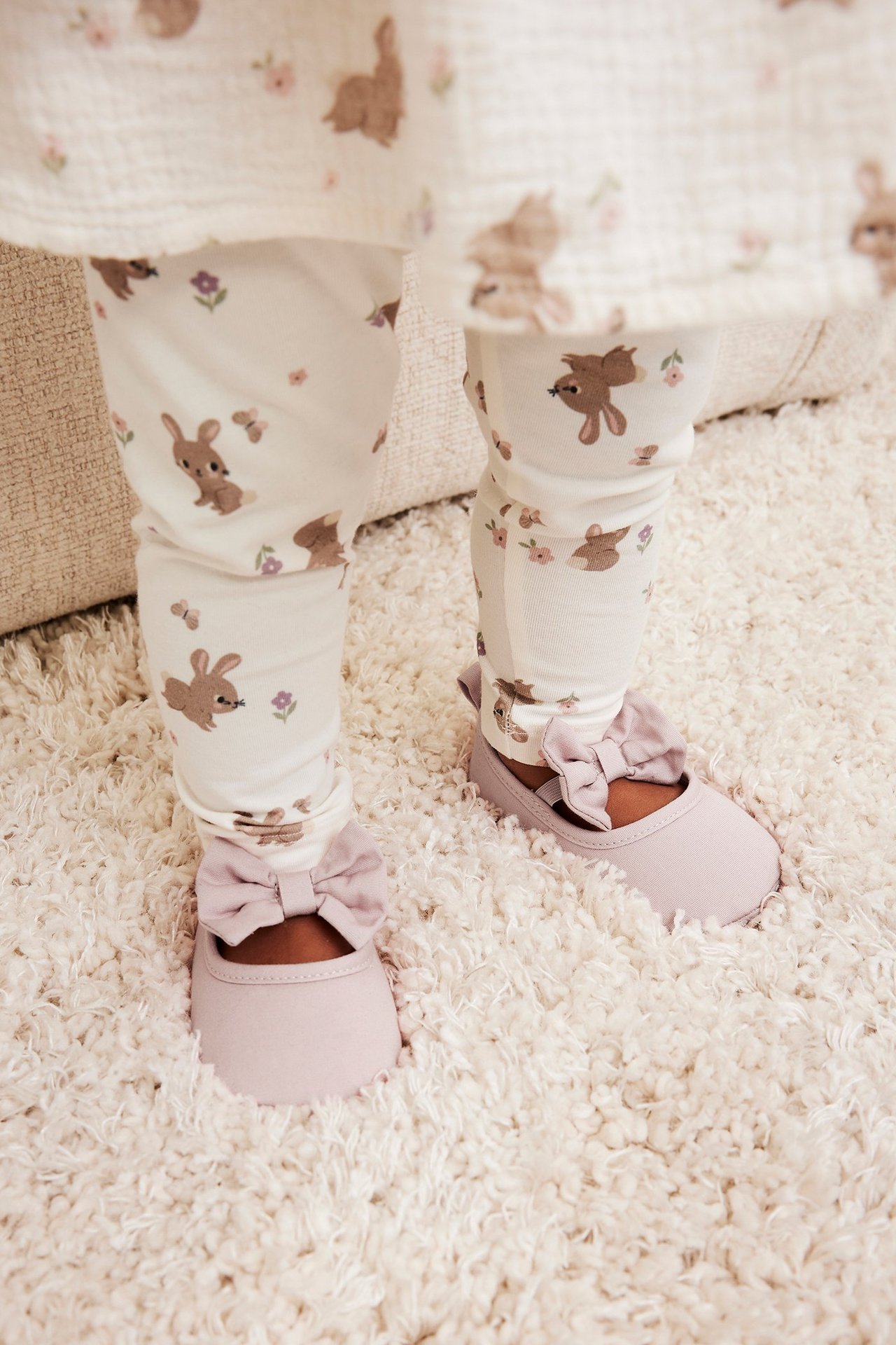 Nærbilde av babyføtter med rosa ballerinasko med sløyfer og hvite leggings med kaninmønster.