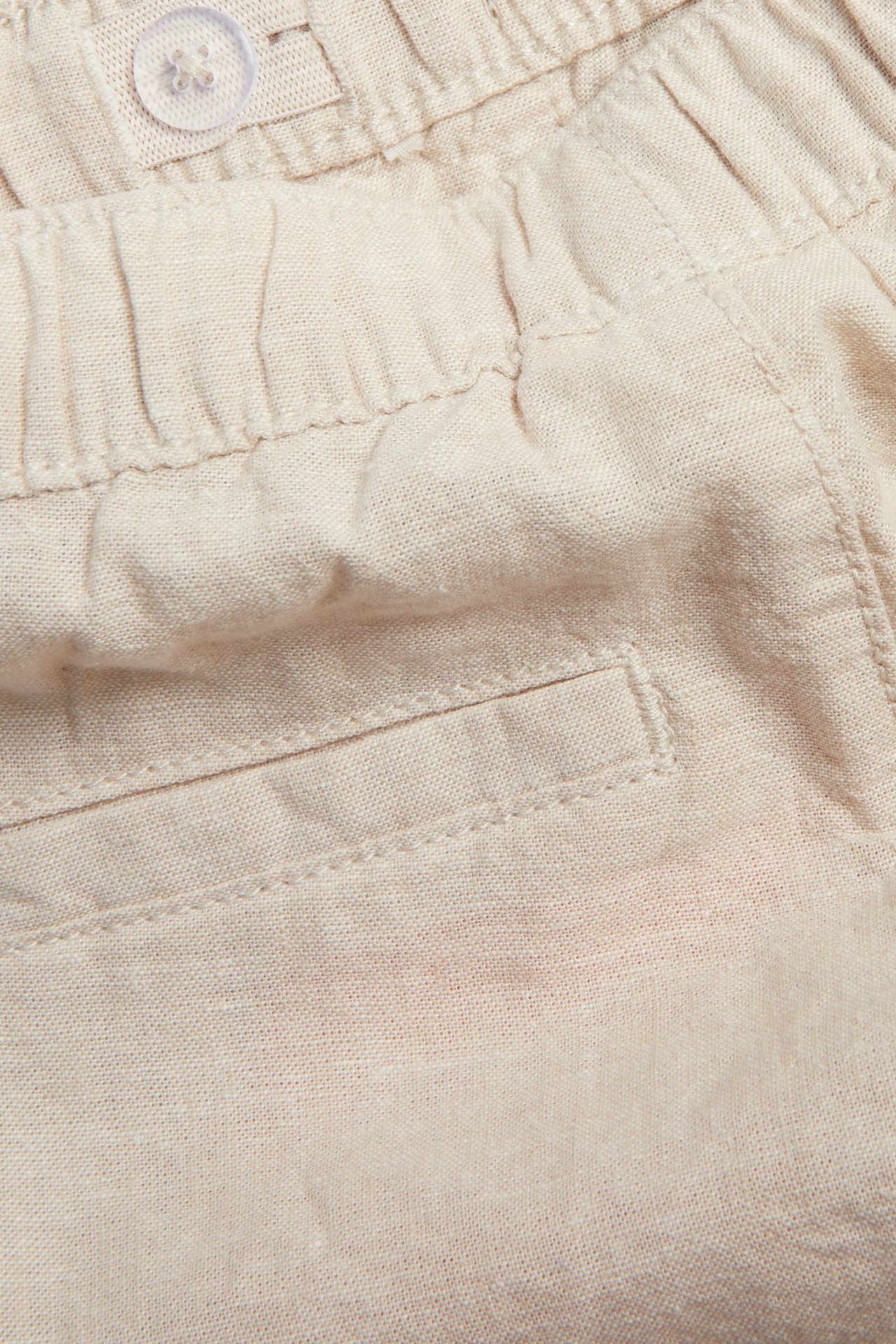Lähikuva: Vaaleanbeiget pellavasekoiteshortsit, joustava vyötärönauha, nappi, takana tekotasku.