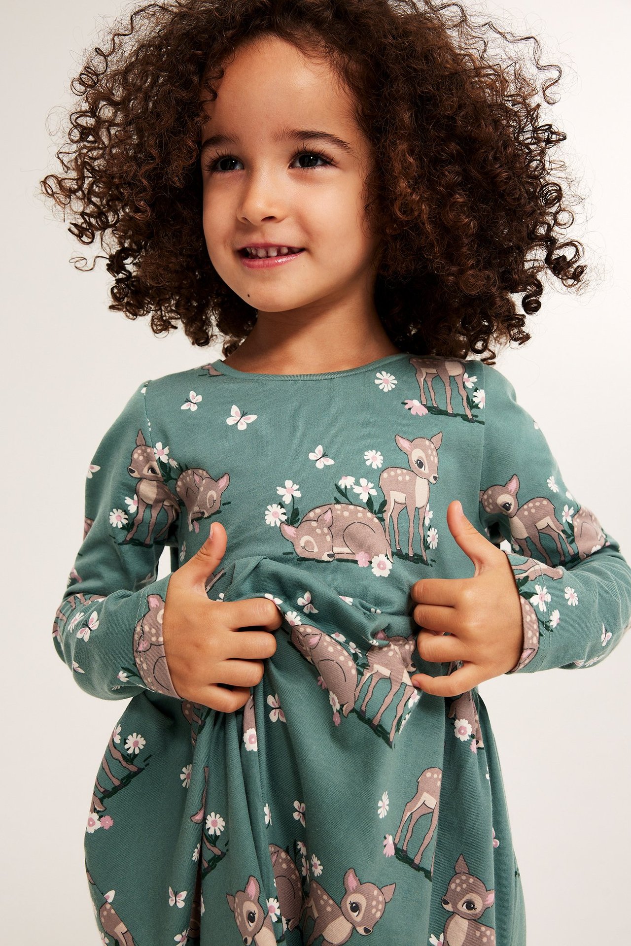 Nærbilde forfra: Barn i grønn bomullsjerseykjole, mønstret med rådyr, sommerfugler og blomster.
