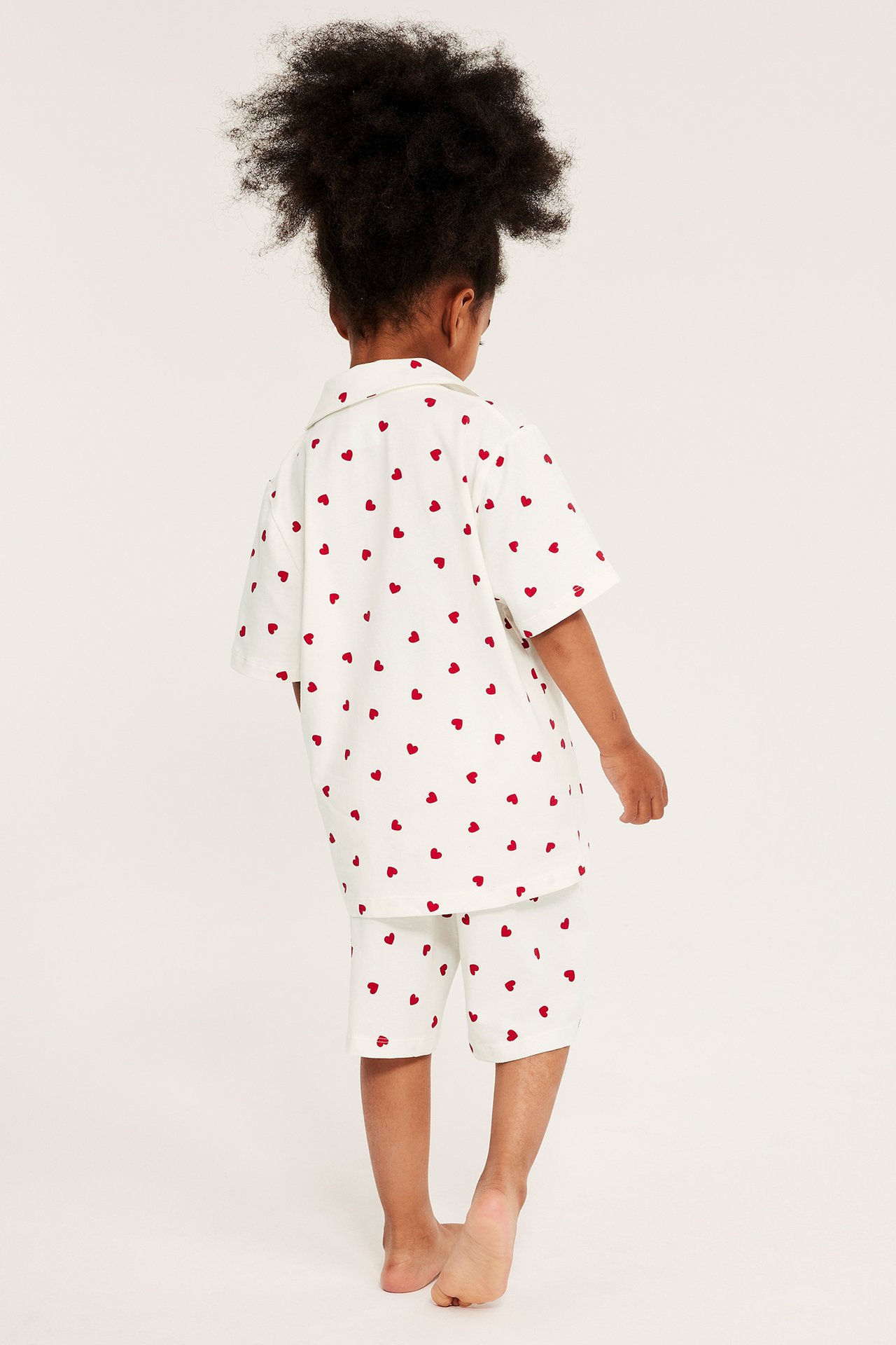 Bakfra: barn i offwhite kortermet pyjamasskjorte med hjerter og matchende shorts.