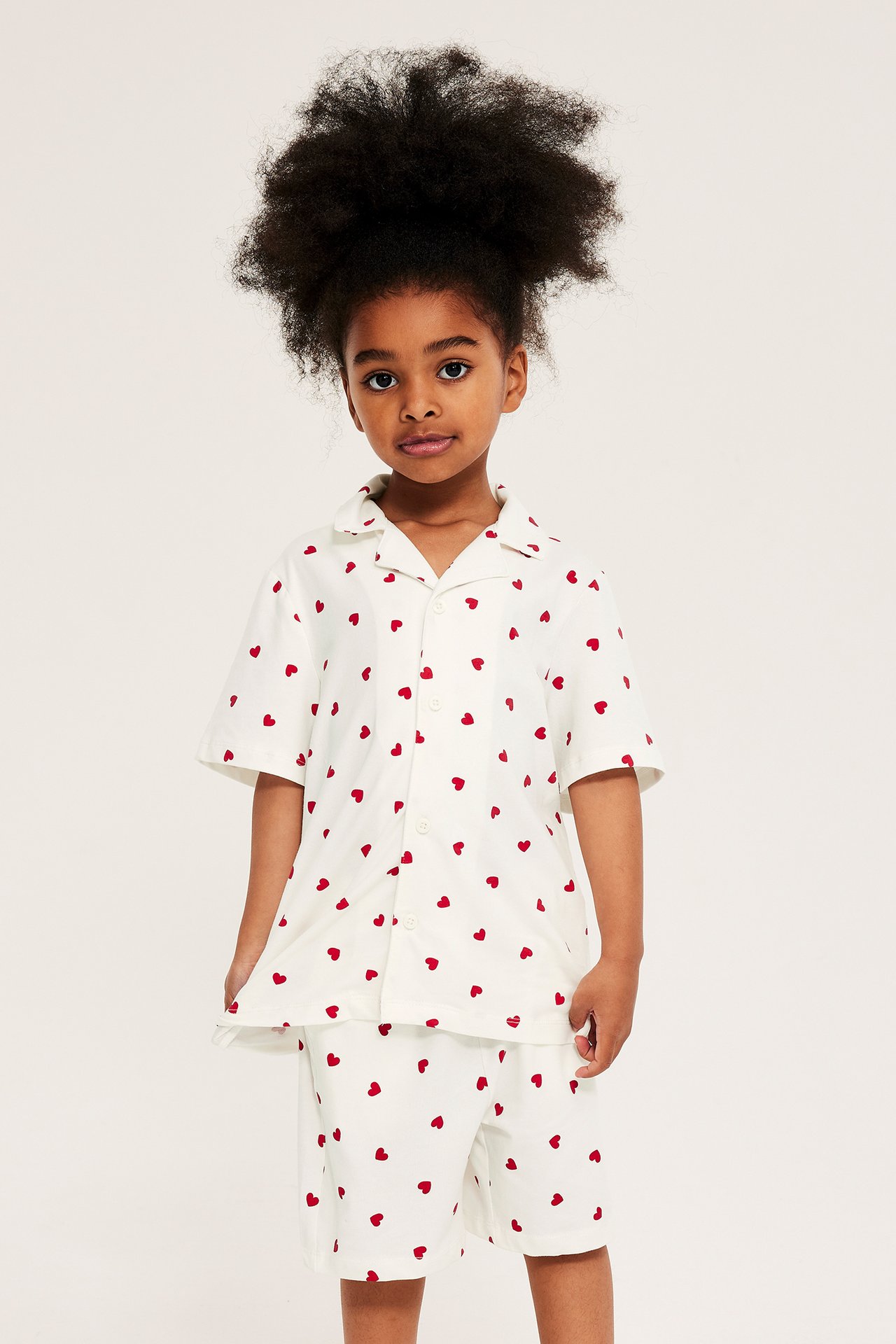 Forfra: Kid har på seg et offwhite pyjamasett med røde hjerter, kortermet skjorte og shorts.