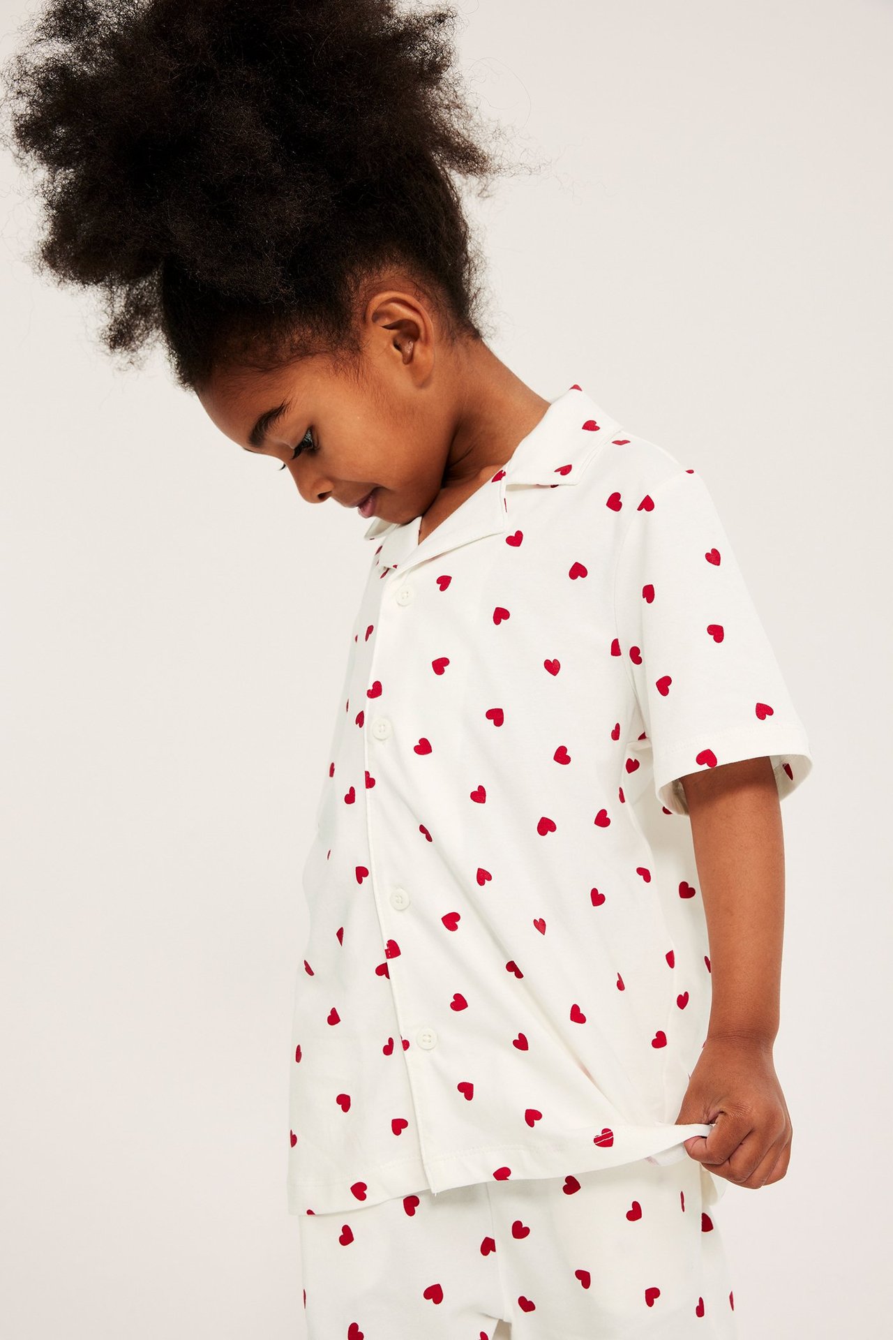 Nærbilde av et barn i en offwhite kortermet pyjamasskjorte og bukse med rødt hjertemønster.