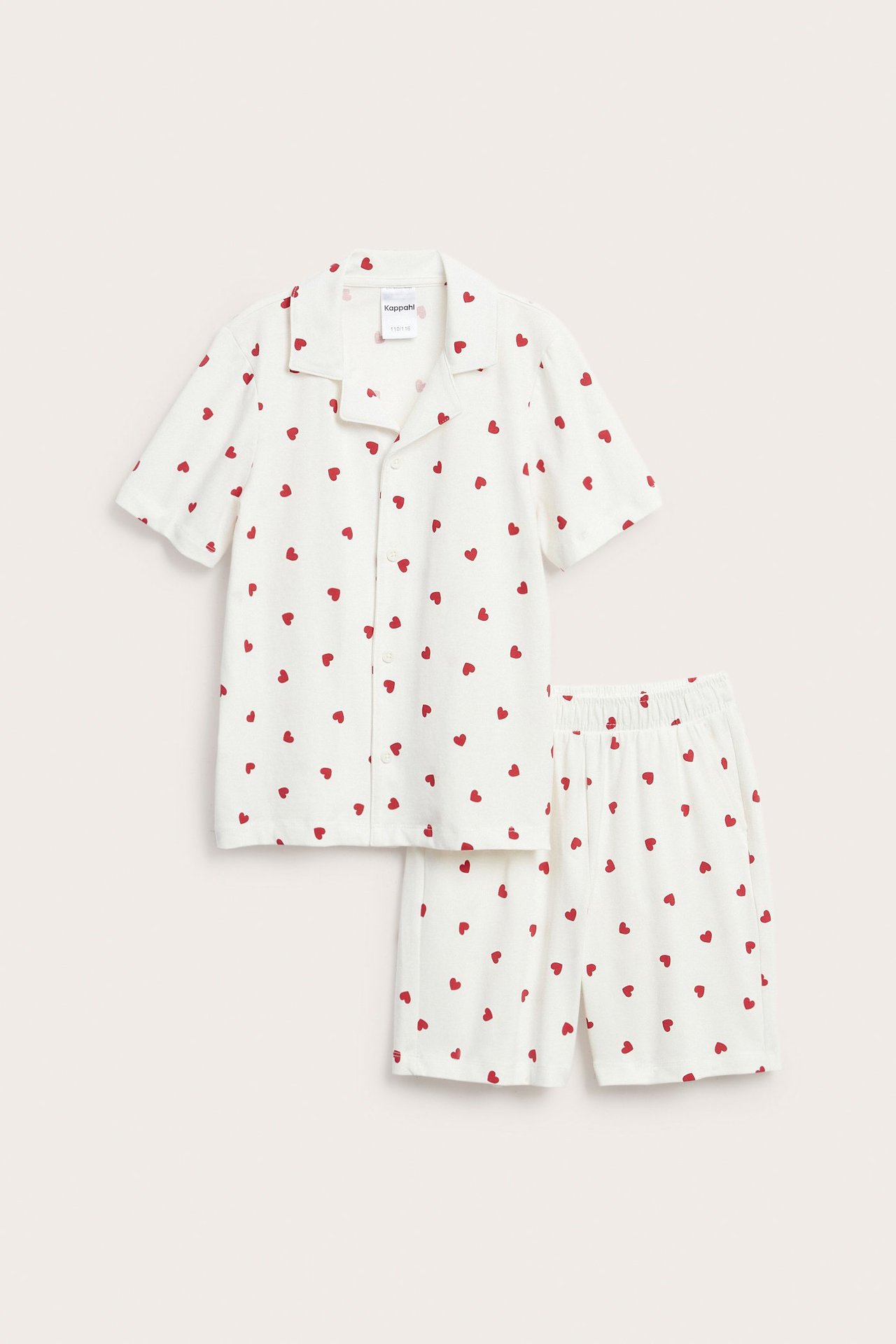 Frontvisning av et off-white pyjamassett med rødt hjertemønster, kortermet topp og matchende shorts.
