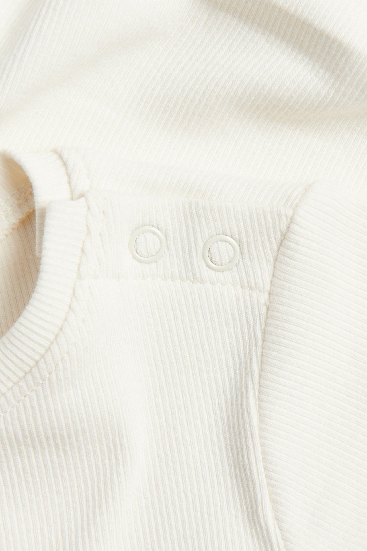 Nærbilde av en offwhite ribbet babybody med trykknapper på skulderen.