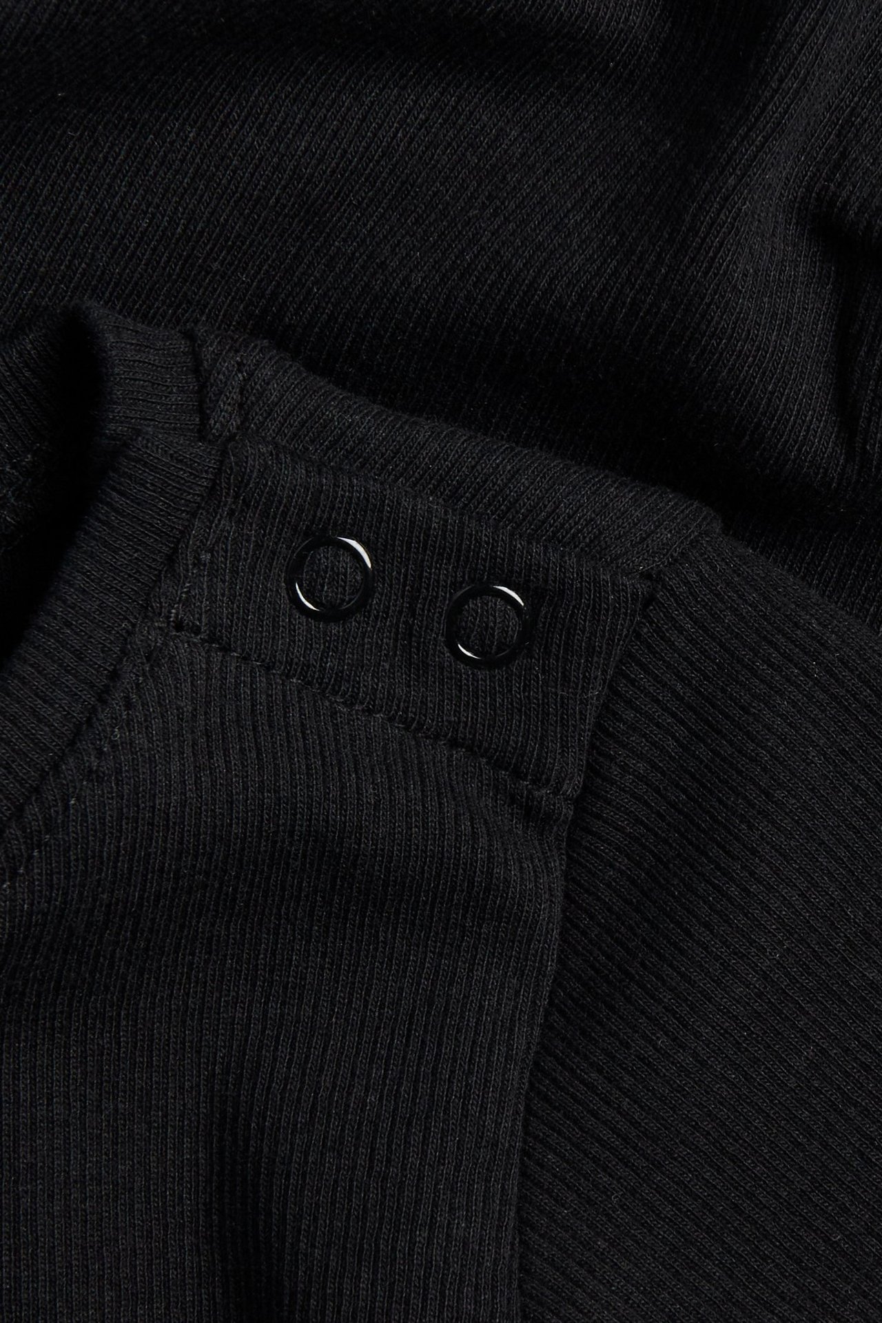 Zbliżenie czarnego prążkowanego body dla niemowląt, ukazujące dwa czarne zatrzaski na ramieniu.