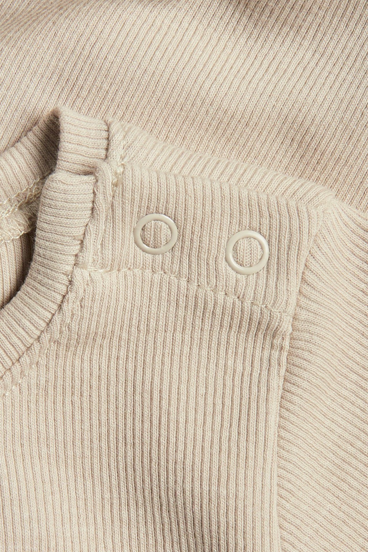 Zbliżenie na beżowe, prążkowane, krótko rękawowe body niemowlęce z dwoma białymi napami na ramieniu.