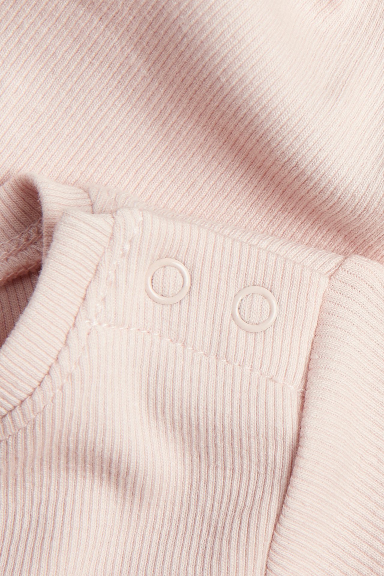 Nærbilde av en rosa kortermet ribbet babybody med hvite trykknapper på skulderen.