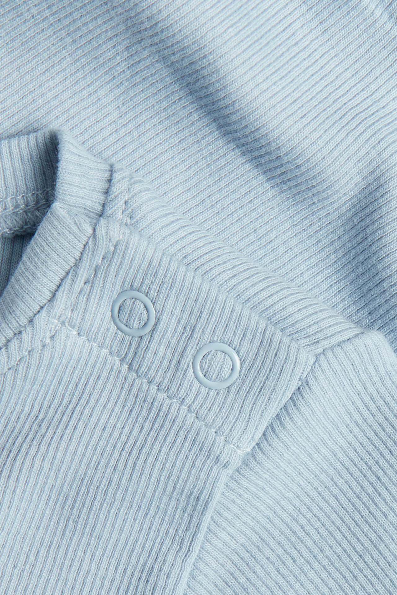 Nærbilde av en lyseblå ribbet babybody med to trykknapper på skulderen.