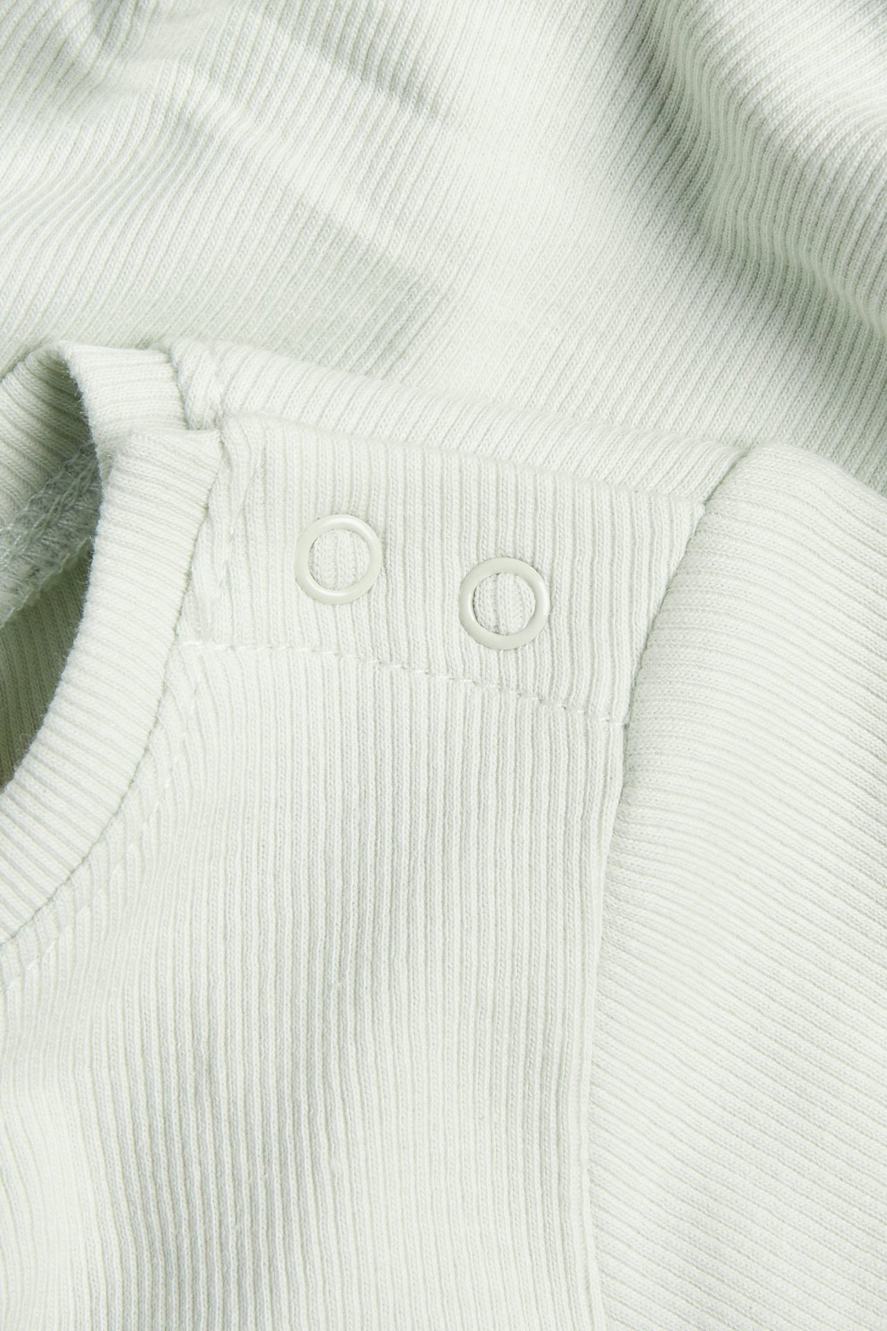 Nærbilde av en lysegrønn ribbet kortermet babybody med to trykknapper på skulderen.