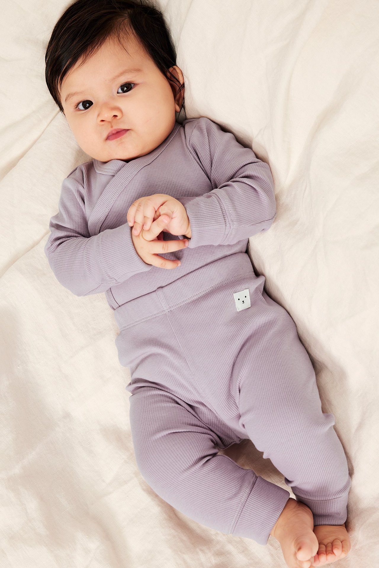 Uppifrånvy av en baby i en lila ribbad omlottbody och matchande ribbade leggings.