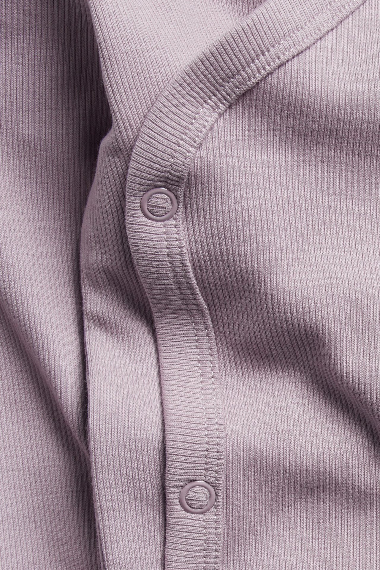 Zbliżenie na liliowe prążkowane body niemowlęce z kopertowym zapięciem na zatrzaski z przodu.