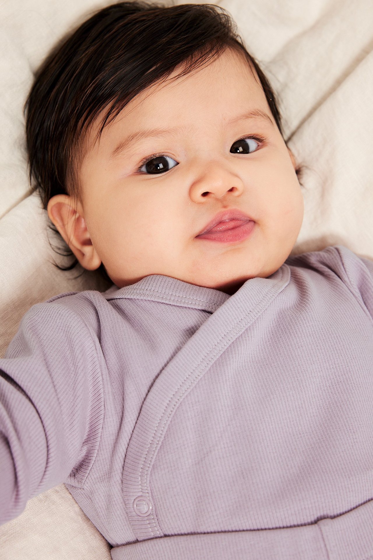 Zbliżenie: niemowlę w liliowym, prążkowanym body kopertowym z zatrzaskami.