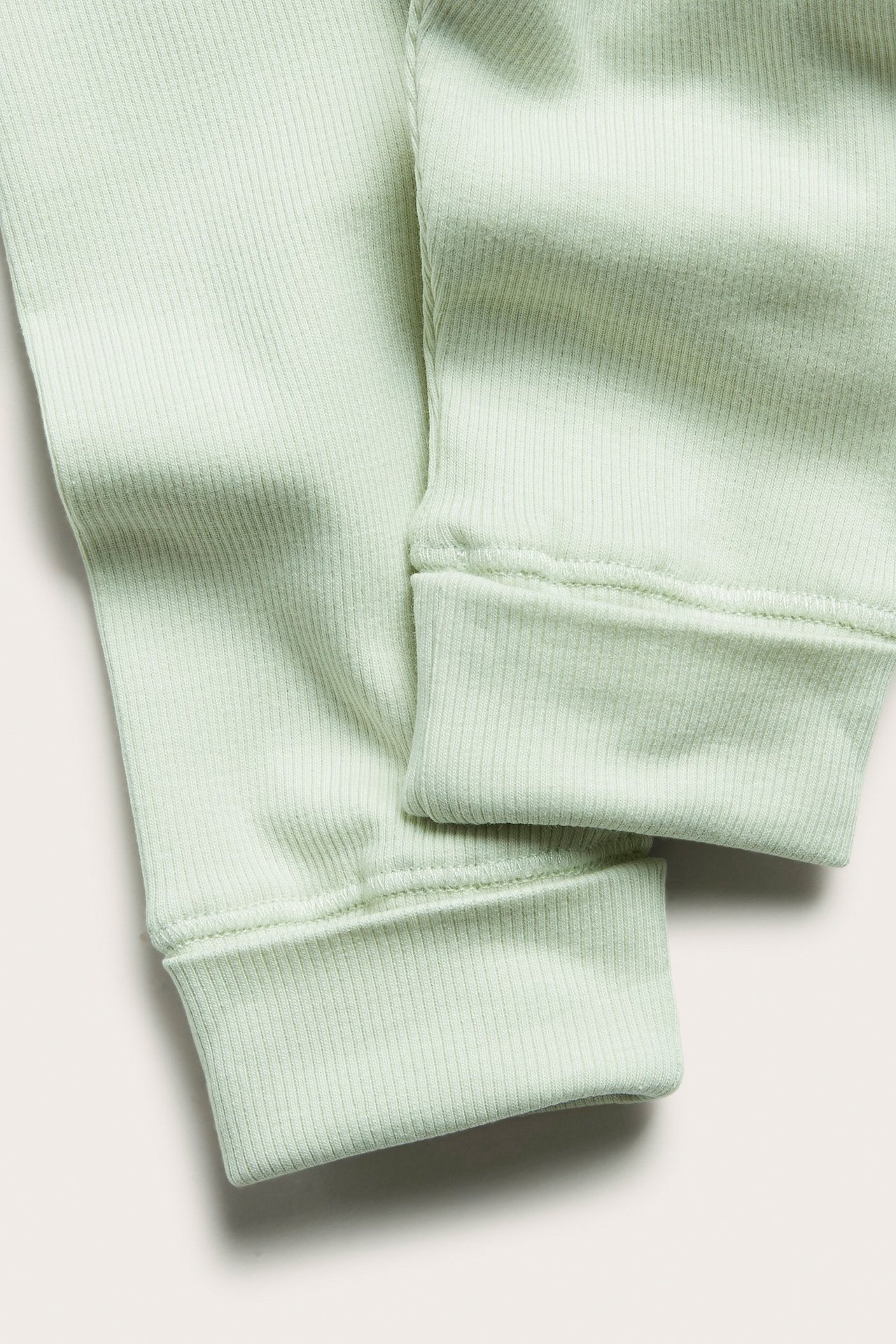 Zbliżenie na jasnozielone prążkowane legginsy z szerokimi, prążkowanymi ściągaczami przy kostkach.