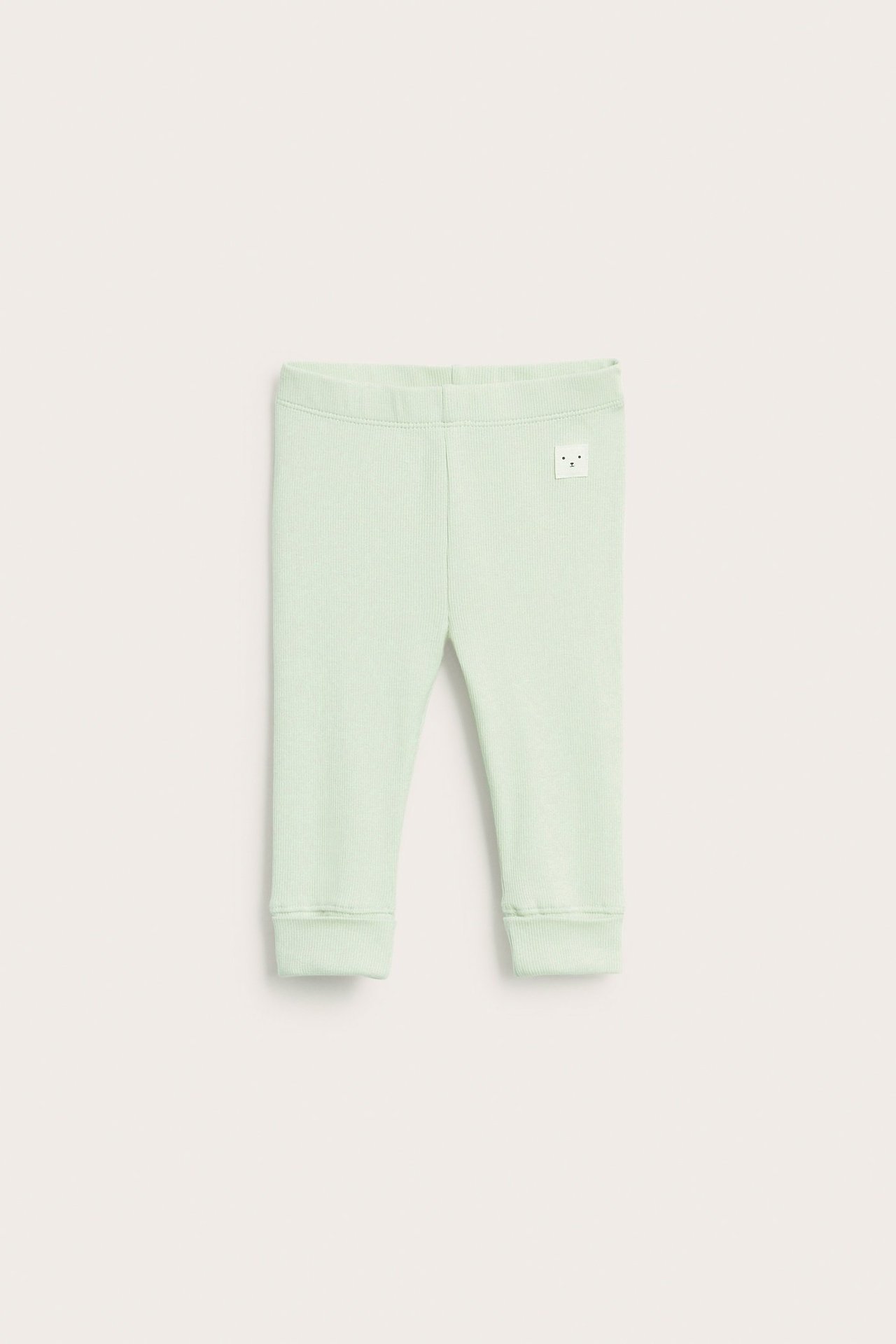 Widok z przodu, jasnozielone prążkowane legginsy niemowlęce z szerokimi mankietami.