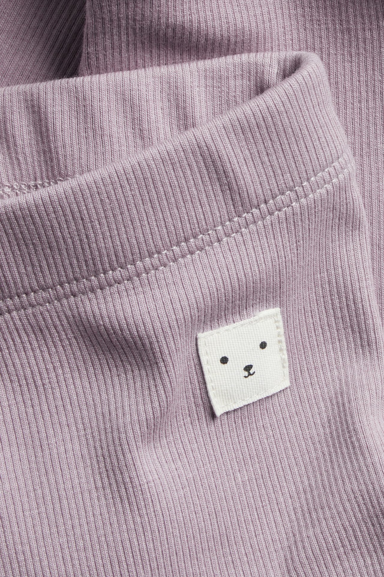 Zbliżenie liliowych prążkowanych legginsów niemowlęcych z małą białą naszywką z misiem.