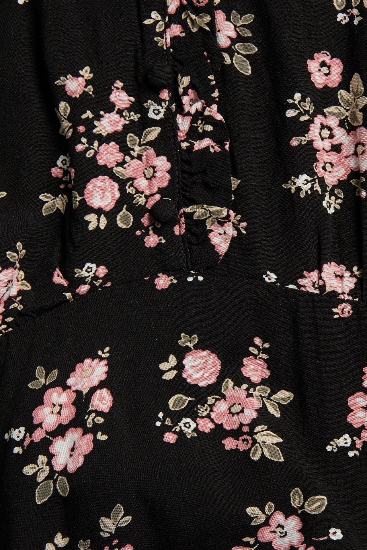 Lähikuva mustasta viskoosimekosta, jossa on vaaleanpunainen kukkakuvio, näyttäen röyhelön ja päällystetyn napin.