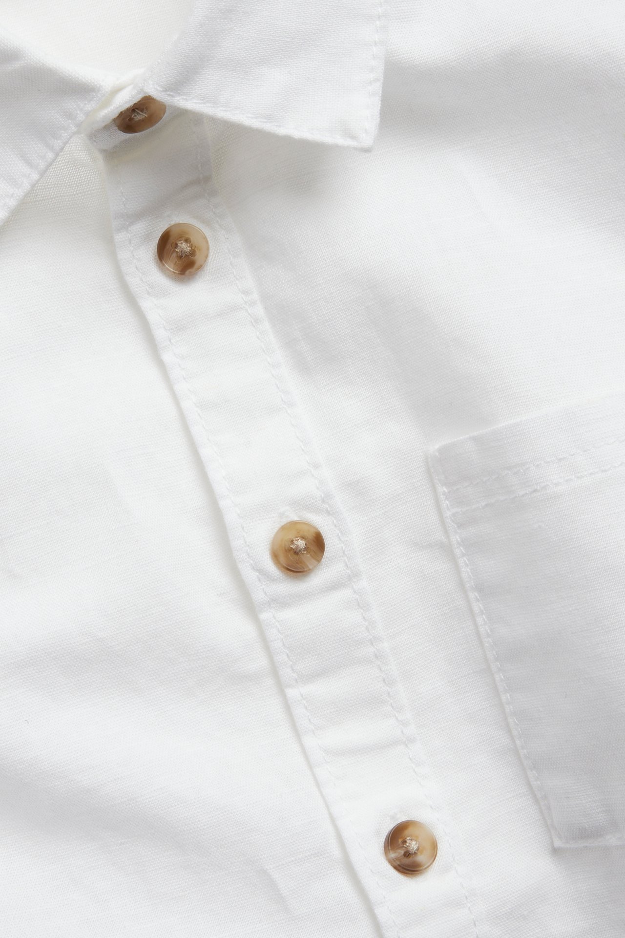 Zbliżenie na białą koszulę z krótkim rękawem z lnu z brązowymi guzikami i kieszenią na piersi.