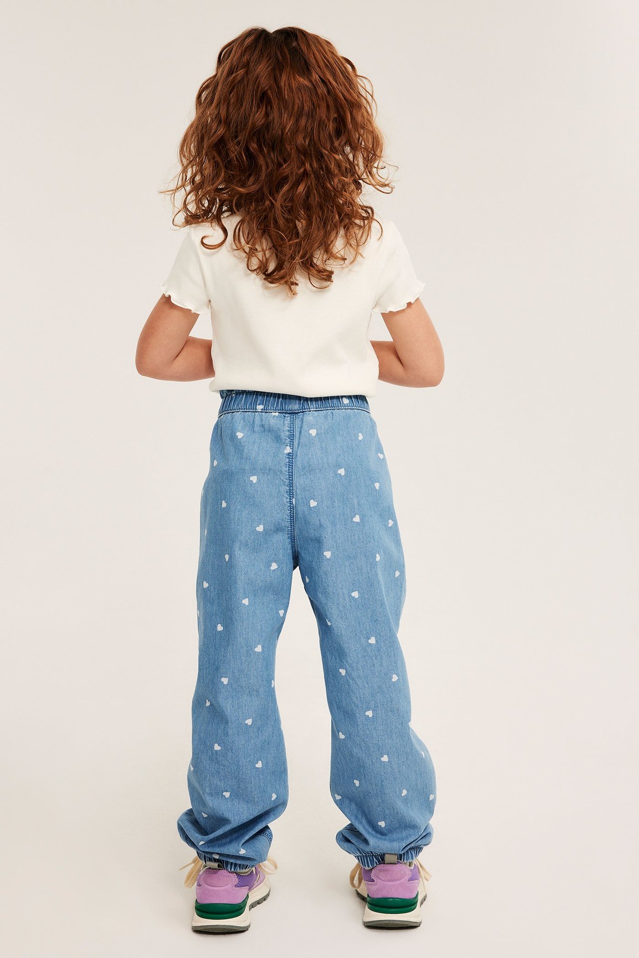 Widok z tyłu dziecka w jasnych jeansach we wzór serc z gumką i białym prążkowanym t-shircie.