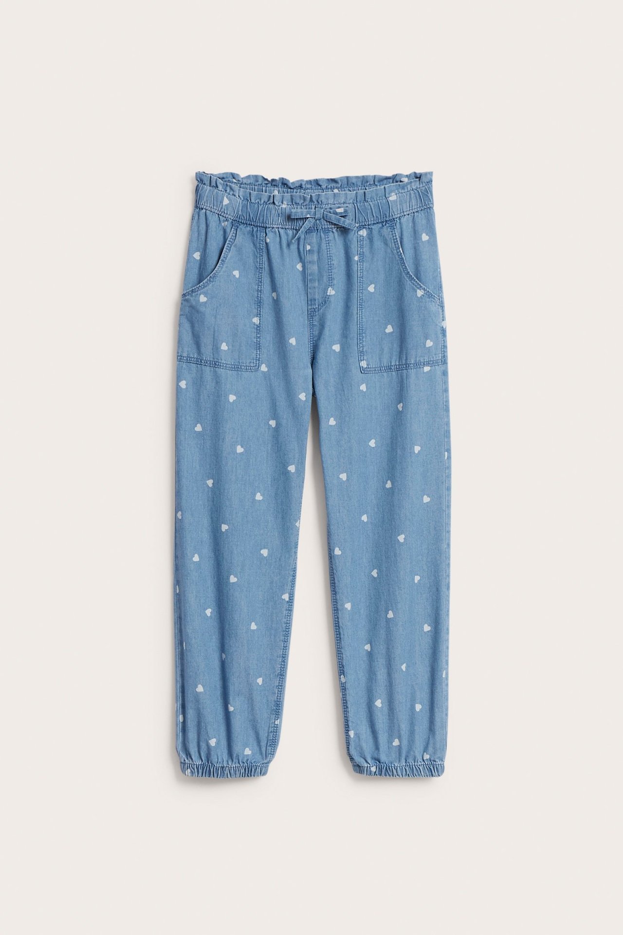 Framifrån: Ljusblåa byxor i mjuk denim för barn, med vita hjärtan, resårmidja och muddar.