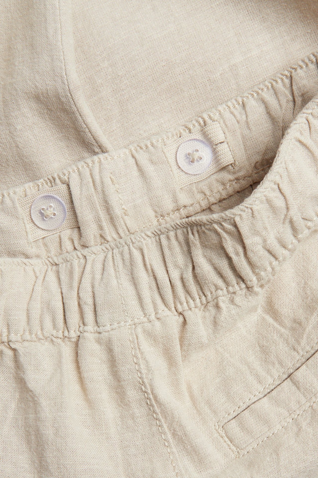 Lähikuva beigestä pellavasekoitehousuista, joissa resori vyötärö ja sisäpuoliset nappisäädöt.