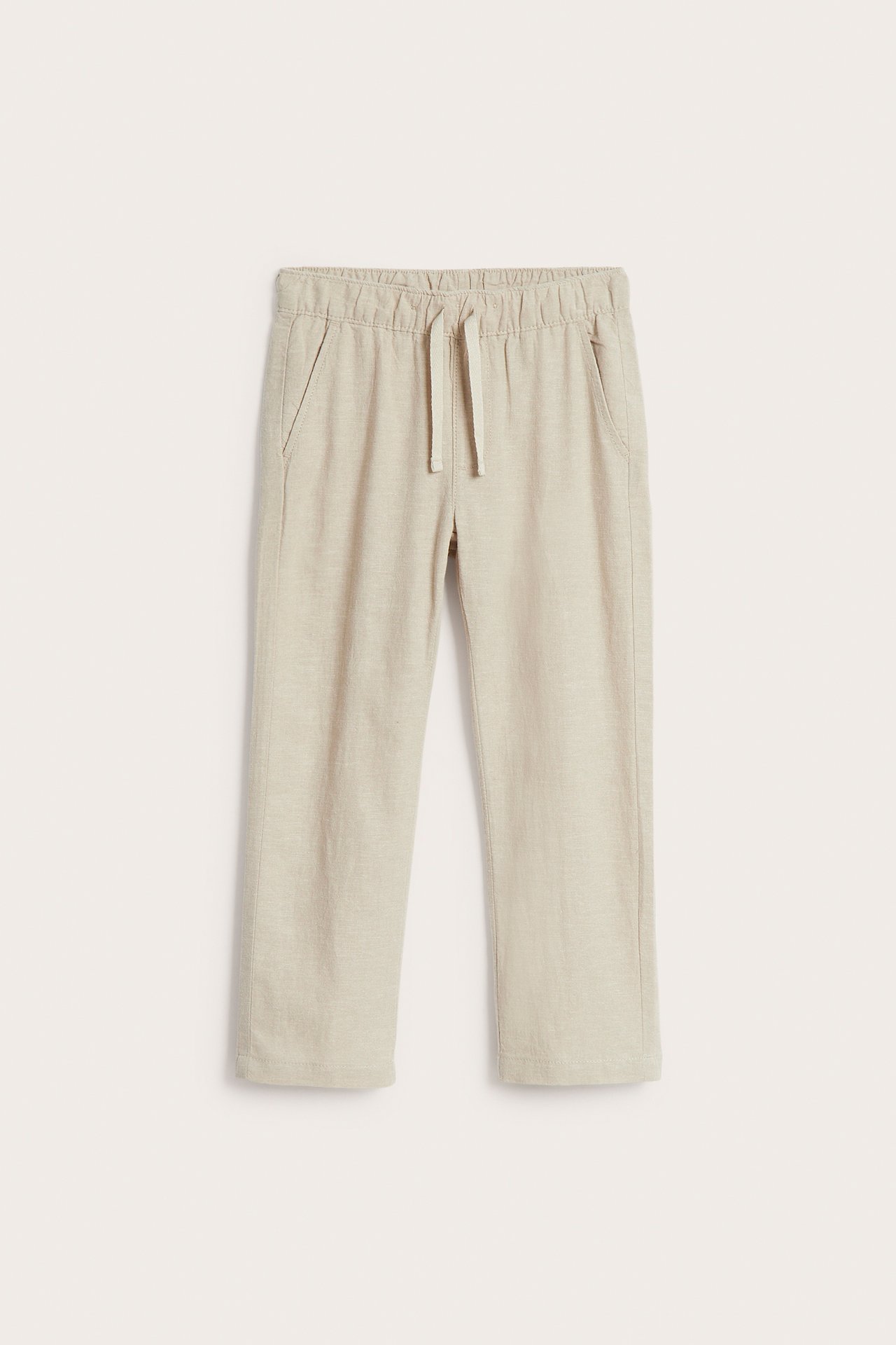 Framifrån: beiga byxor i linnemix för barn med resårlinning, dragsko och sidofickor.