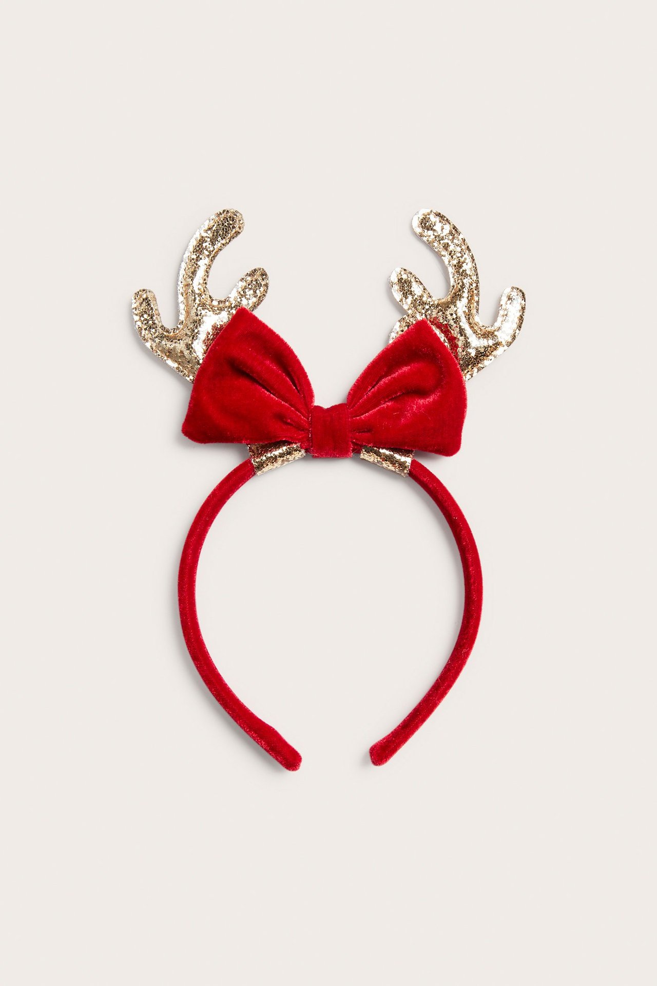 Framifrån, ett rött sammetsdiadem med röd sammetsrosett och guldfärgade glittriga renhorn.