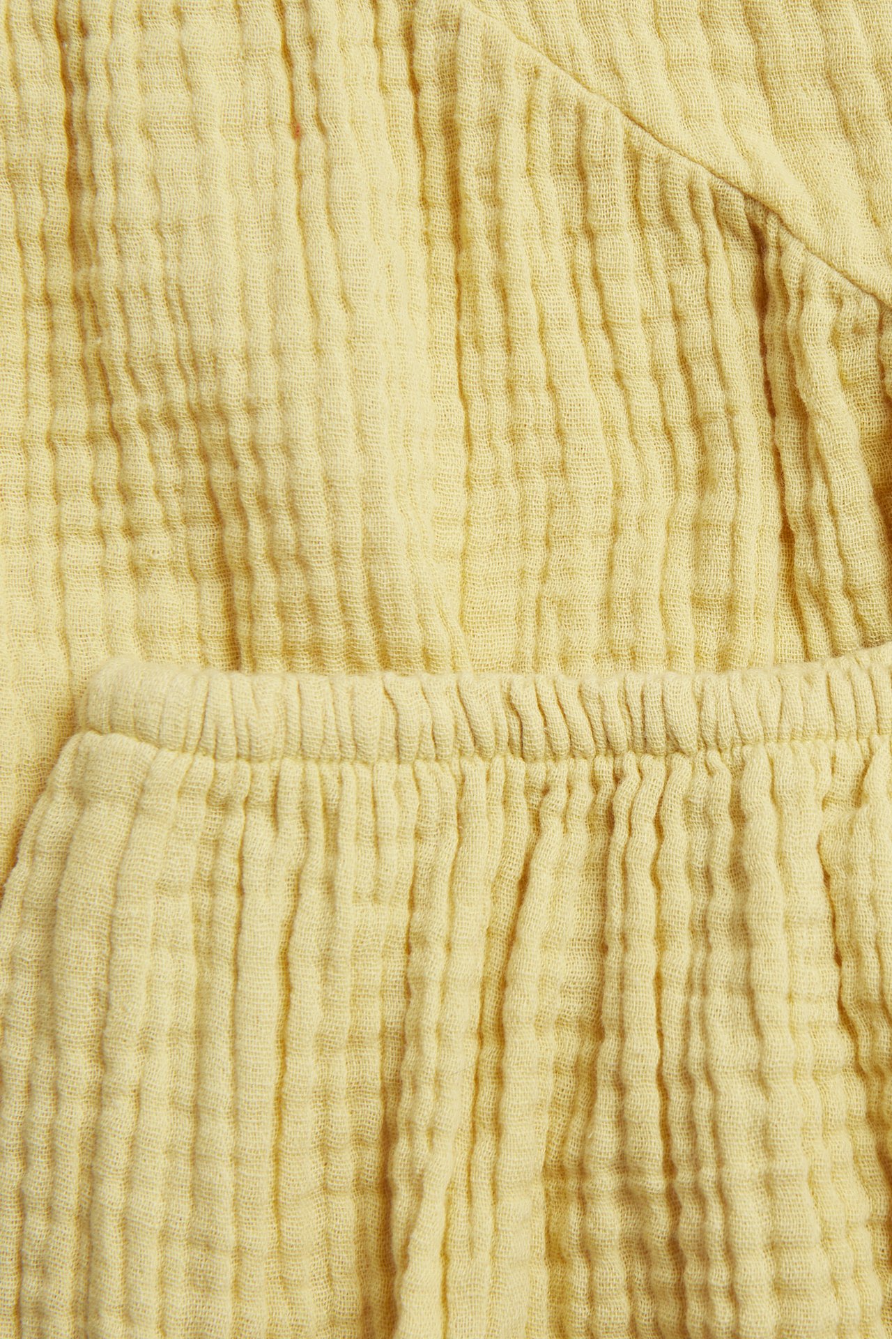 Närbild: gult skrynkligt muslintyg från babyklänning och bloomer med resårlinning.