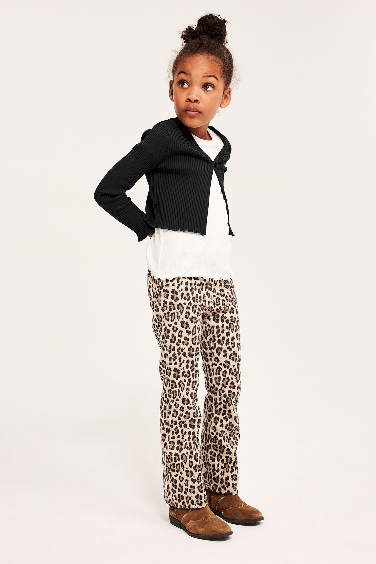 Barns svarta ribbade croppade bolero med knapp, över vit t-shirt och leopardmönstrade byxor, sidovy.