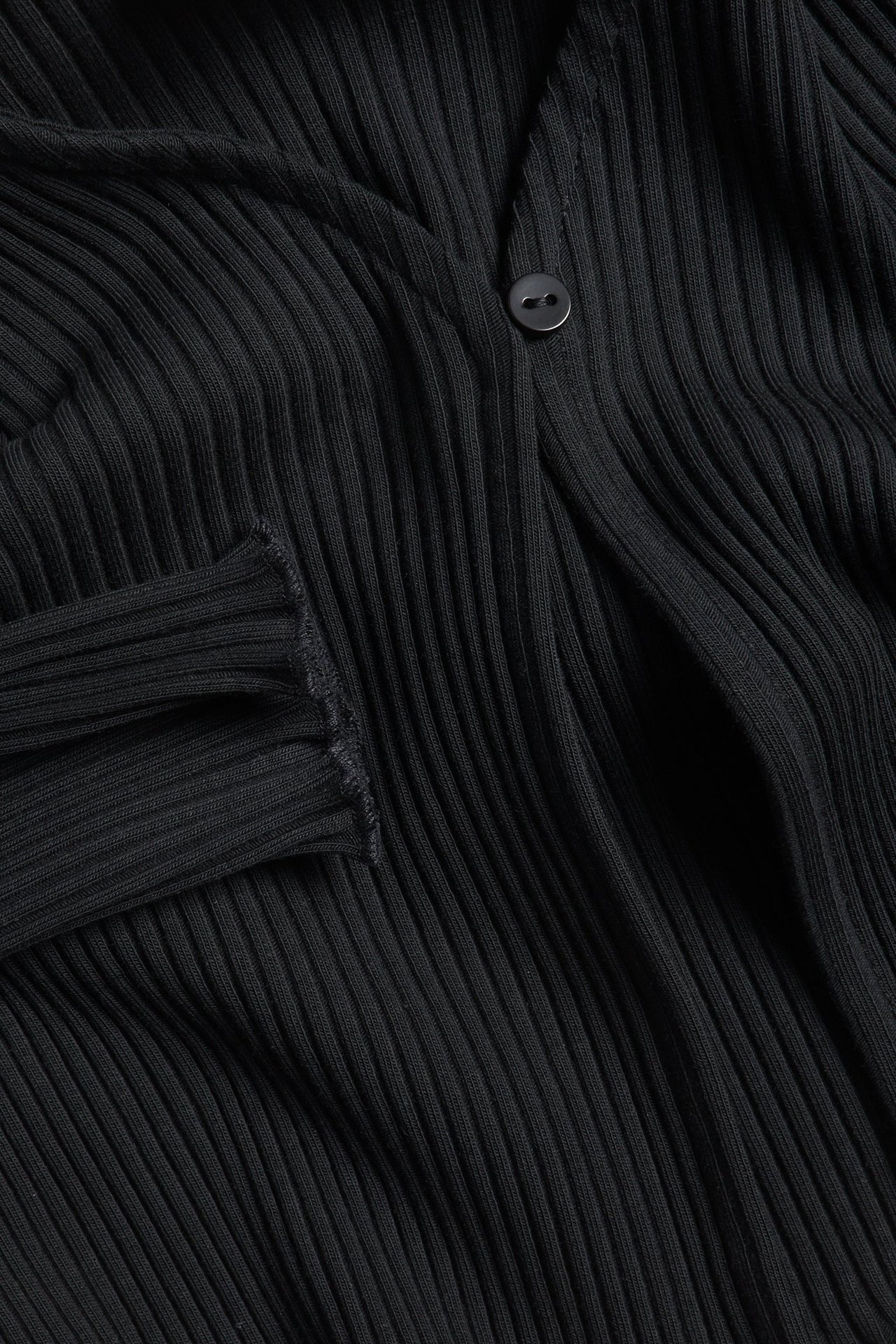 Zbliżenie czarnego, prążkowanego bolerka z mieszanki bawełny z jednym guzikiem z przodu.