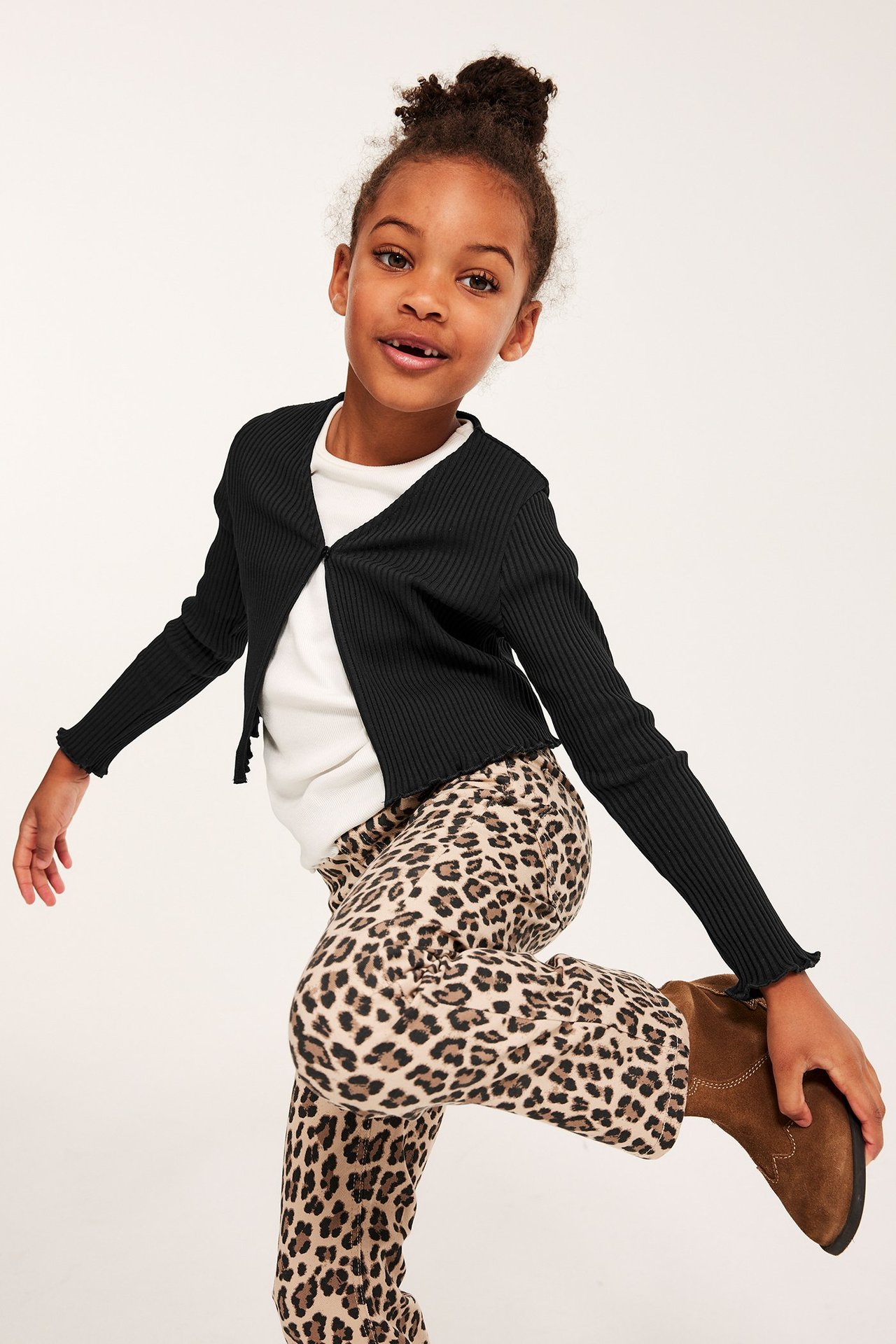 Dziecko w czarnym prążkowanym bolerku, białym topie, spodniach w panterkę i brązowych butach.