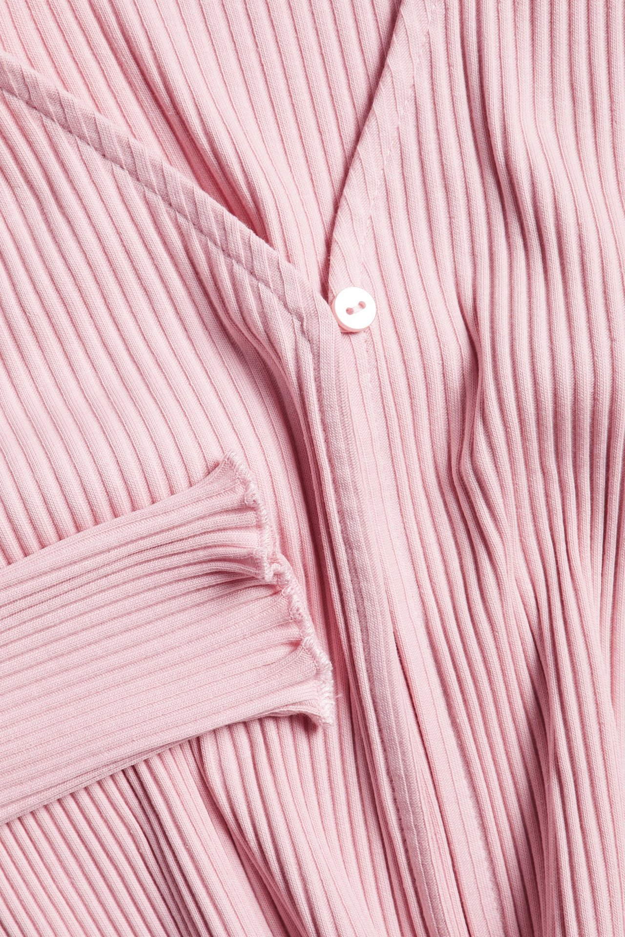 Zbliżenie jasnoróżowego prążkowanego bawełnianego bolerka o krótkim kroju z białym guzikiem z przodu.