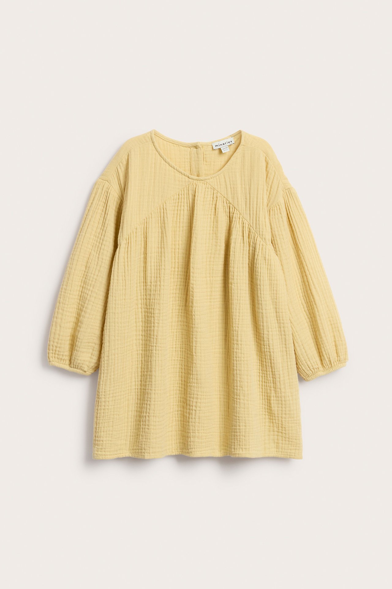 Framsida av gul lös muslin klänning med rynkad ok och trekvarts puffärmar.